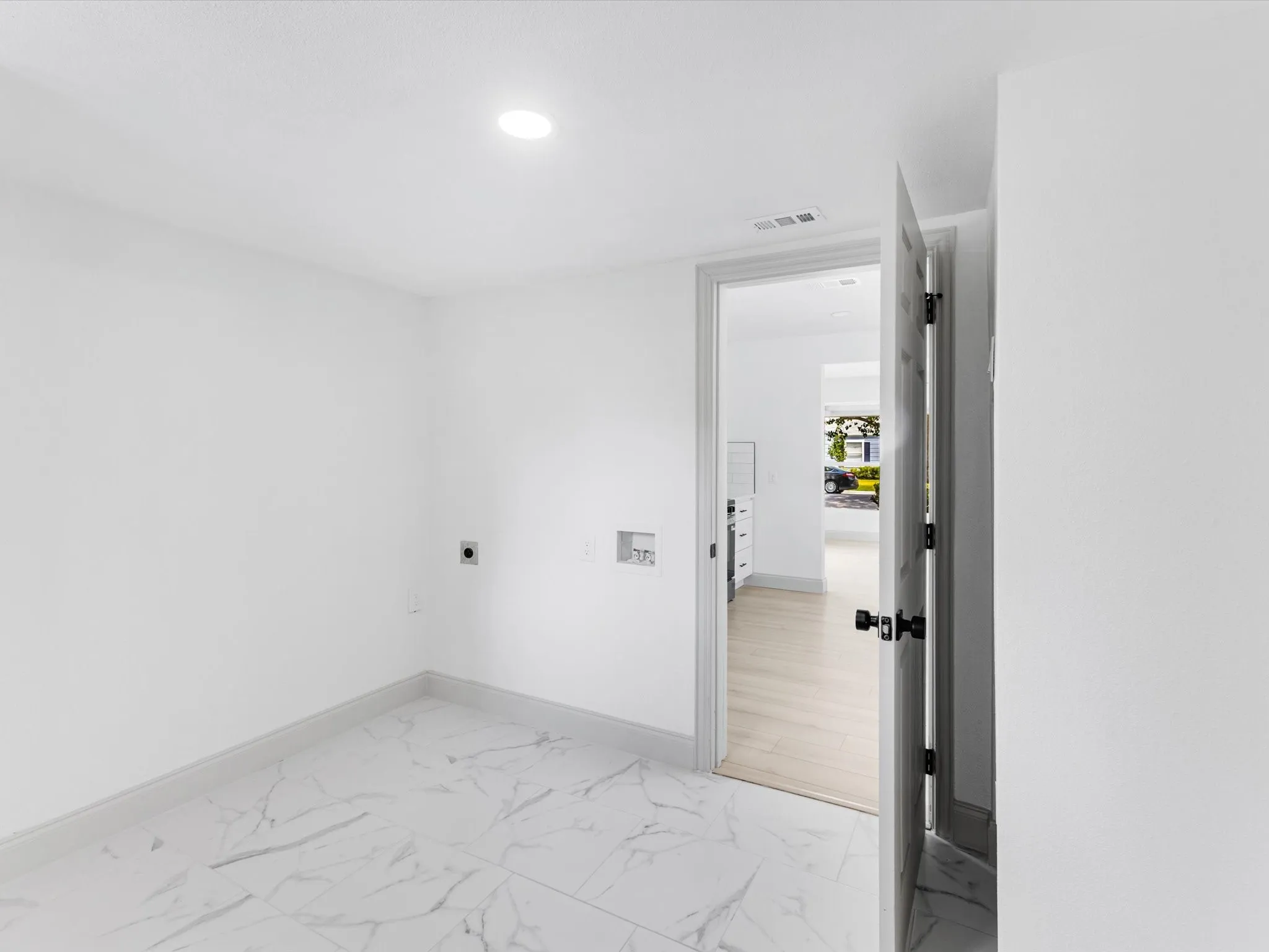 Laundry area featuring white walls, large format marble-look tile flooring, and a recessed ceiling light