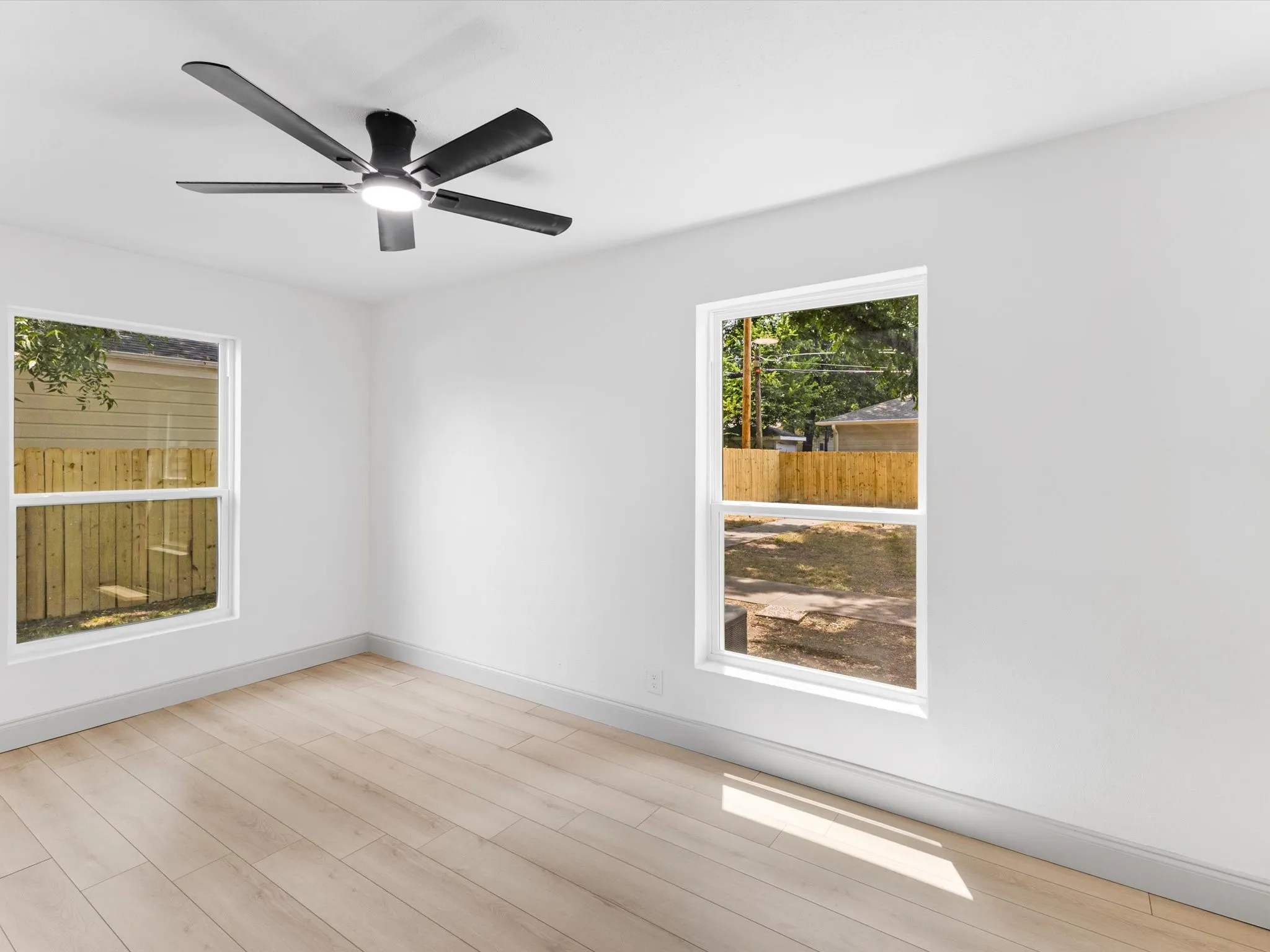 Bright room featuring two windows with white trim, wood-finish flooring, and a contemporary ceiling fan with integrated lighting