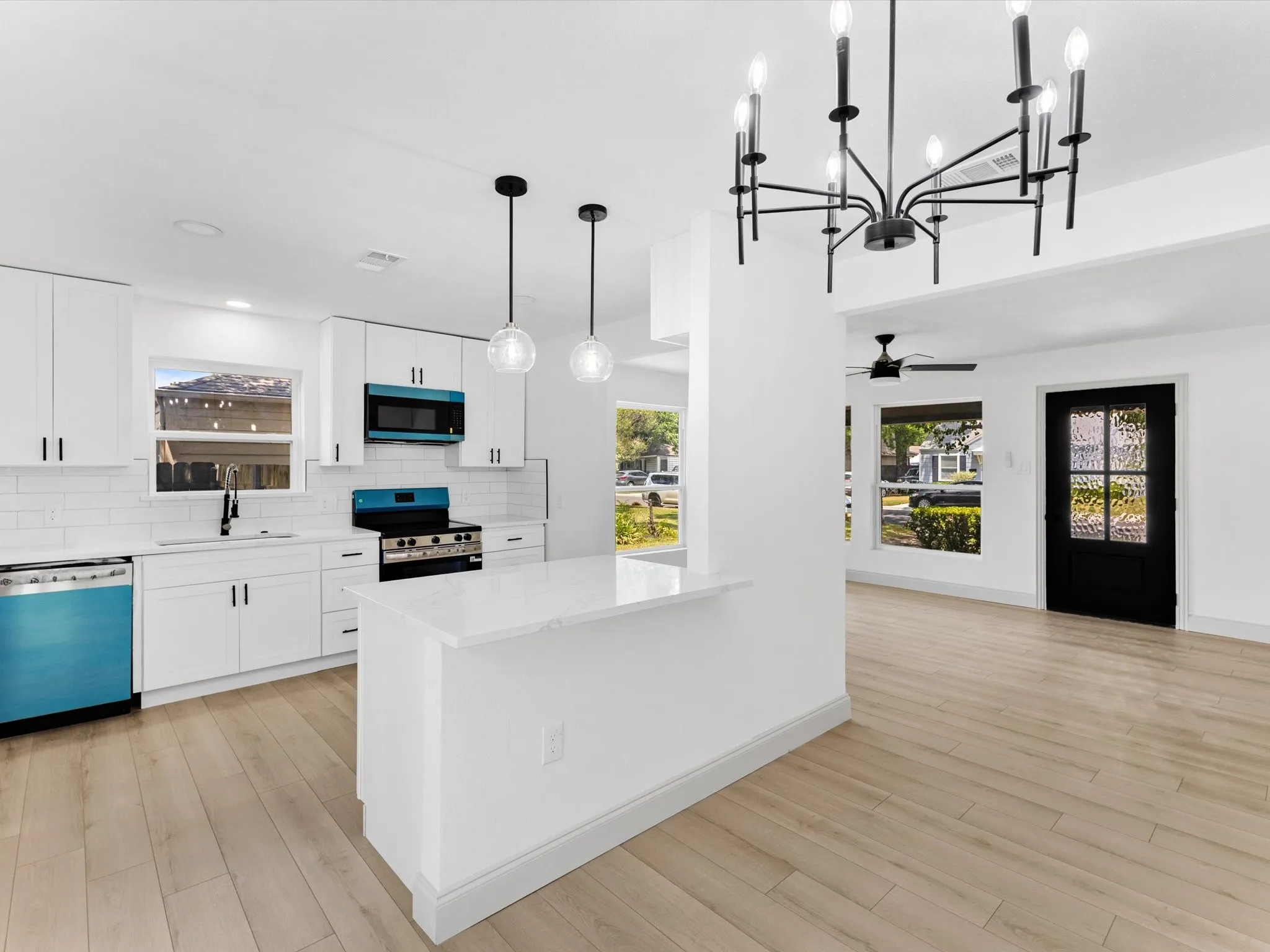 Open-concept living area featuring light wood-finish flooring, white walls, and a modern black chandelier