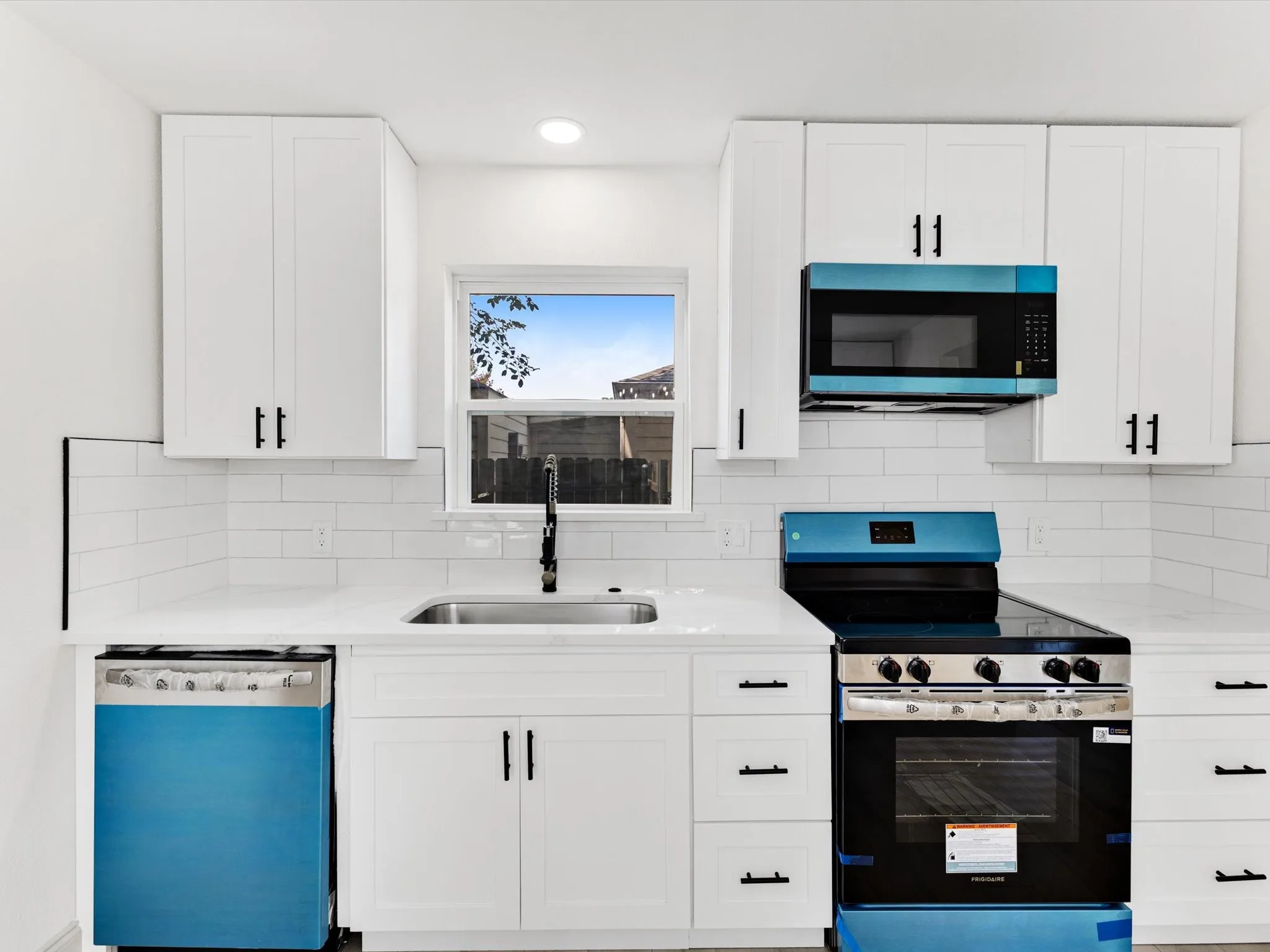 Modern kitchen featuring white shaker cabinetry with matte black hardware, white subway tile backsplash, white countertops, and a stainless steel sink with a black faucet