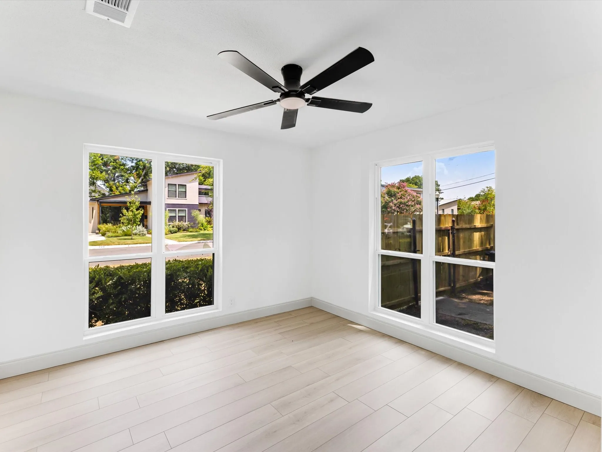Bright room featuring a contemporary ceiling fan, dual large windows, light wood-finish flooring, white walls, and white baseboards