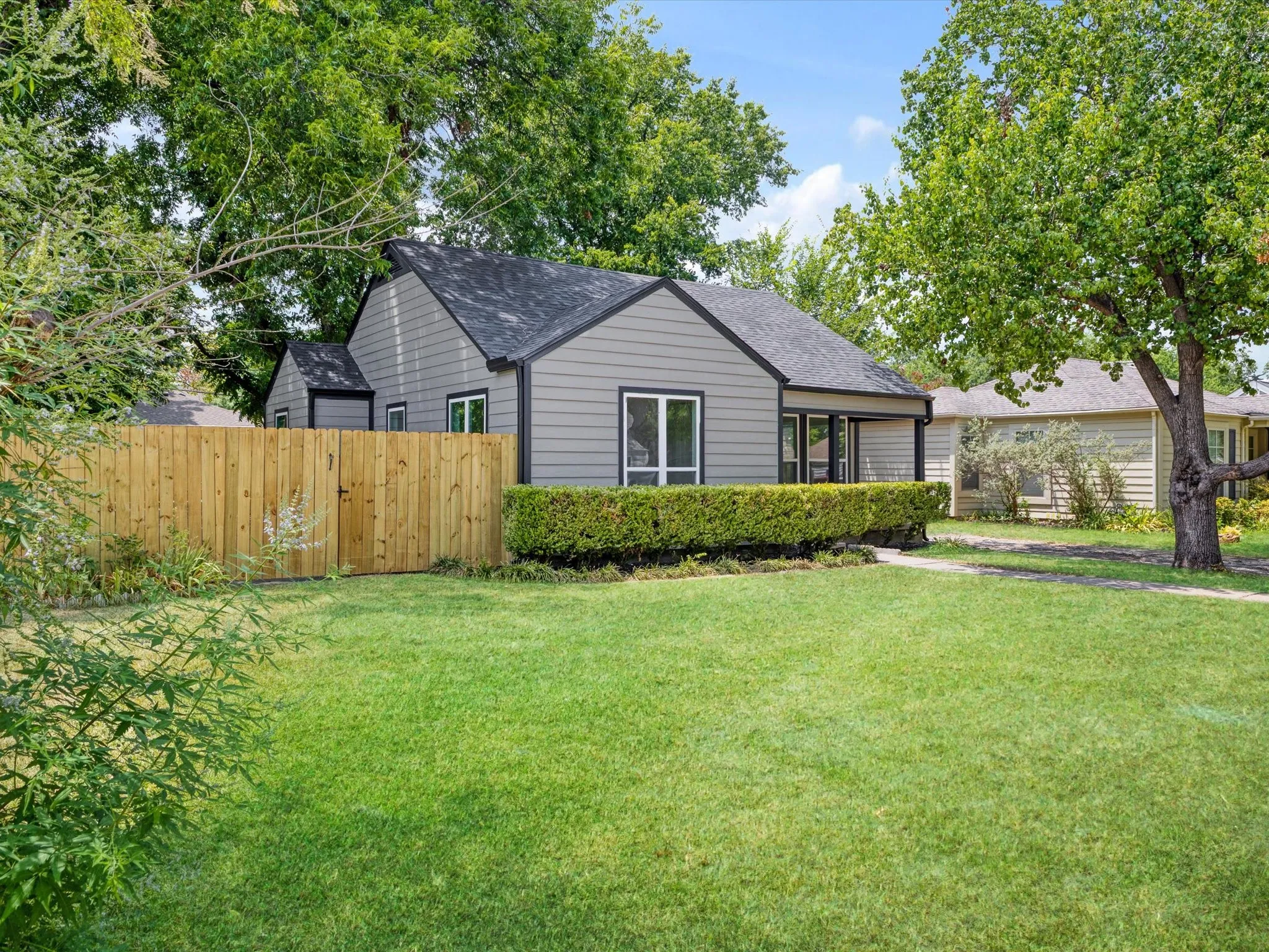 Gray siding exterior with black trim, a dark shingle roof, and a mature tree providing shade