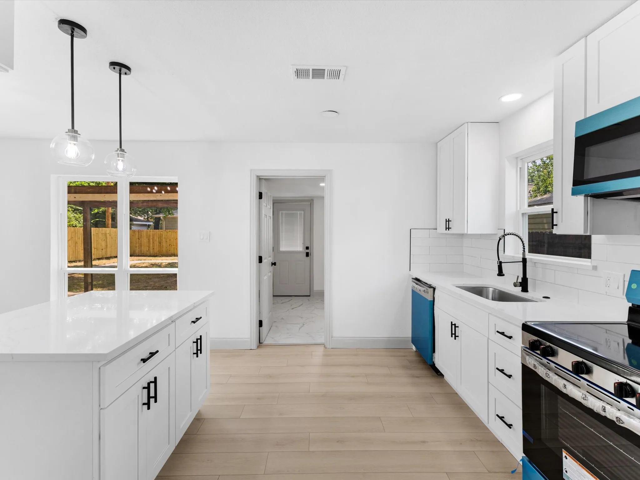 Kitchen featuring a center island with pendant lighting, light wood-finish flooring, white cabinetry with black hardware, white subway tile backsplash, and a stainless steel sink with a black faucet