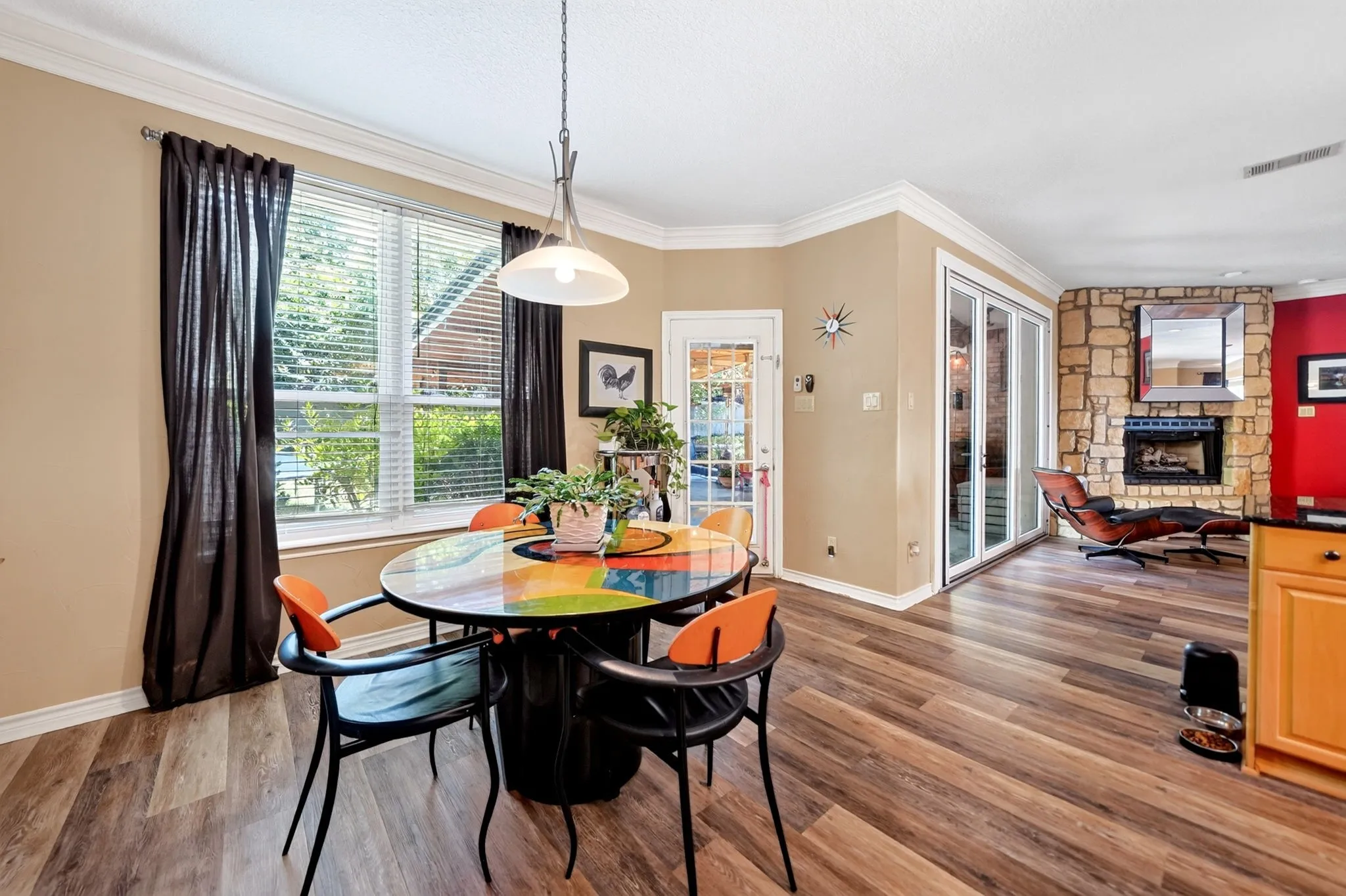 Open-concept living space featuring wood-finish flooring, a stone-faced fireplace with a mantel, and crown molding