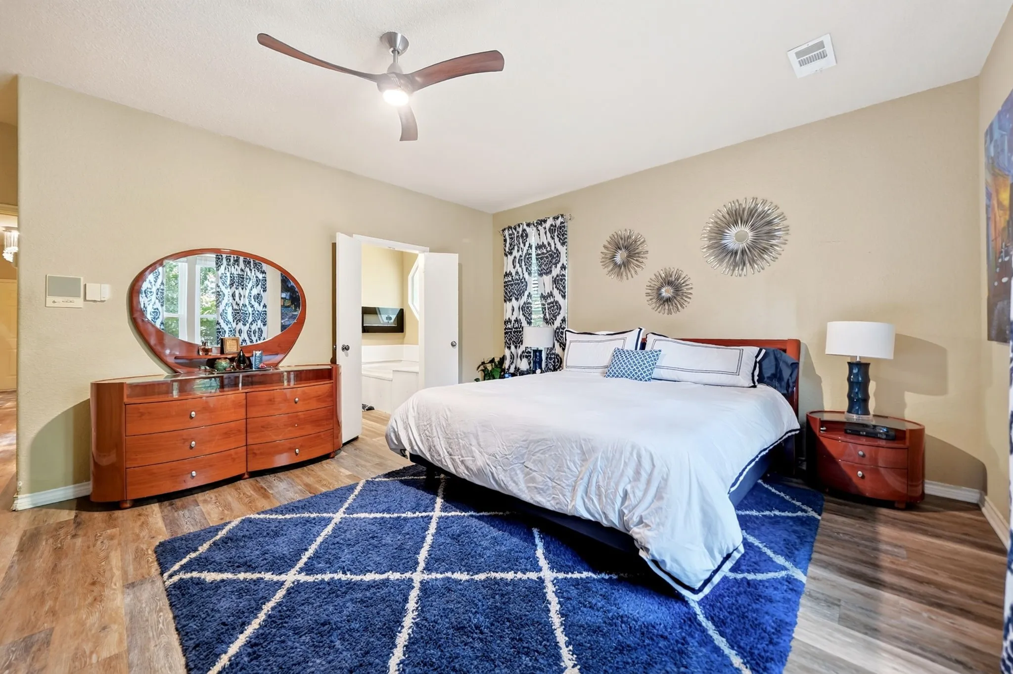 Spacious bedroom featuring wood-finish flooring, a contemporary ceiling fan with integrated lighting, and neutral wall tones