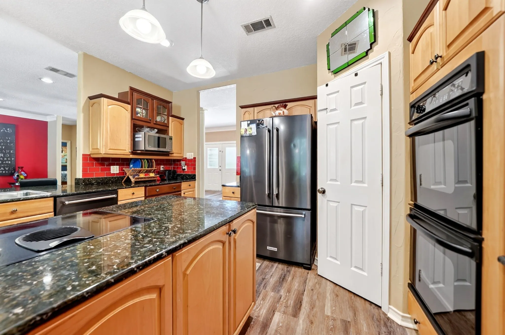 Kitchen featuring a large island with cooktop, granite-style countertops, wood cabinetry, stainless steel appliances, and wood-finish flooring