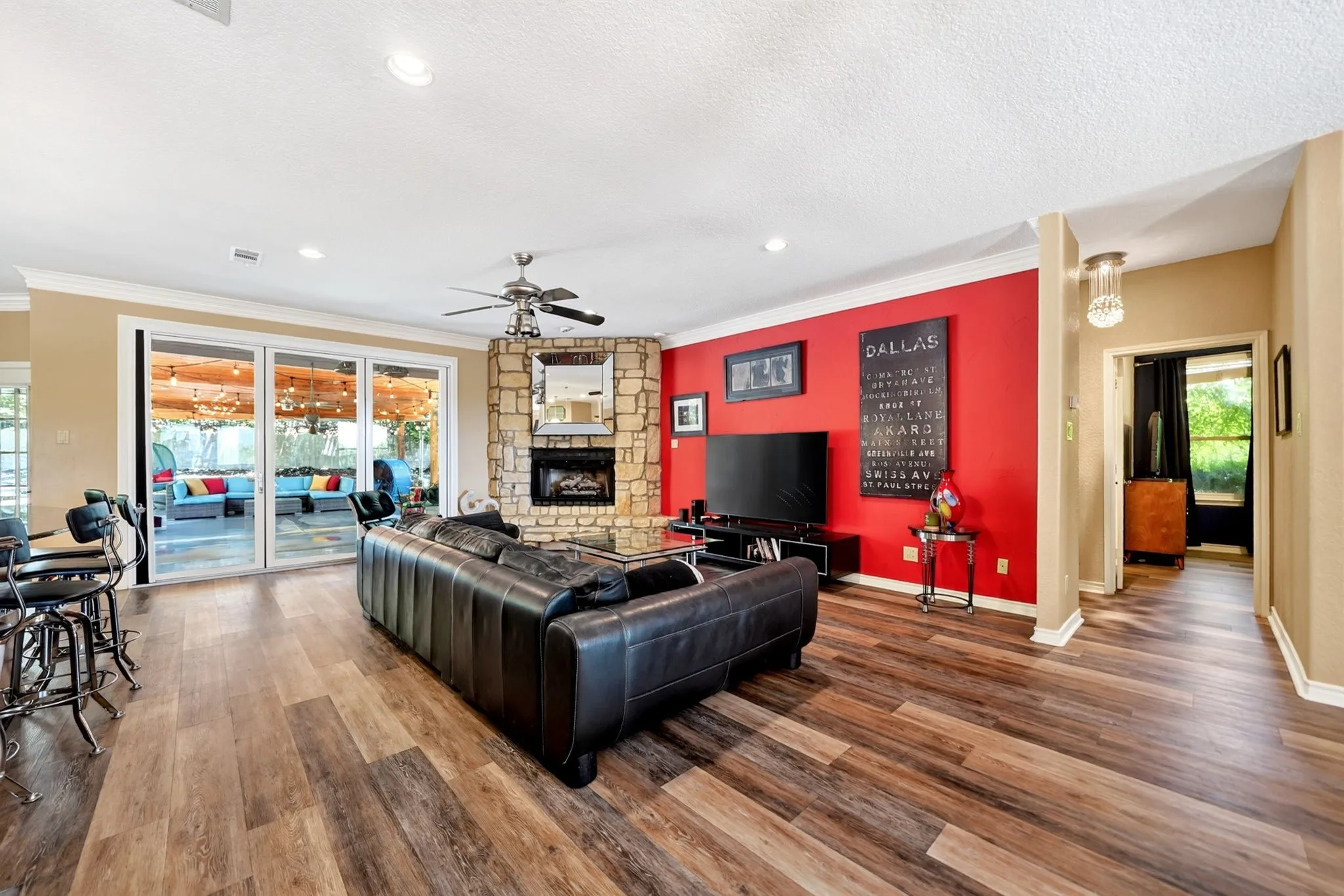Spacious living area featuring wood-finish flooring, a stone-clad fireplace, and an exposed beam ceiling