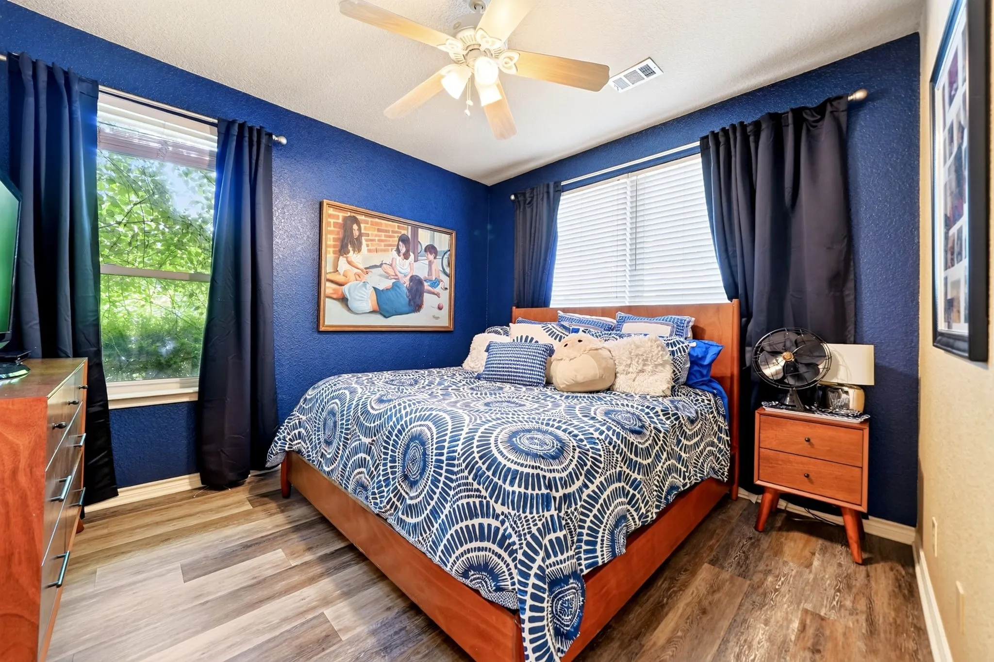 Room featuring wood-finish flooring, a ceiling fan, and two windows with blinds and curtains