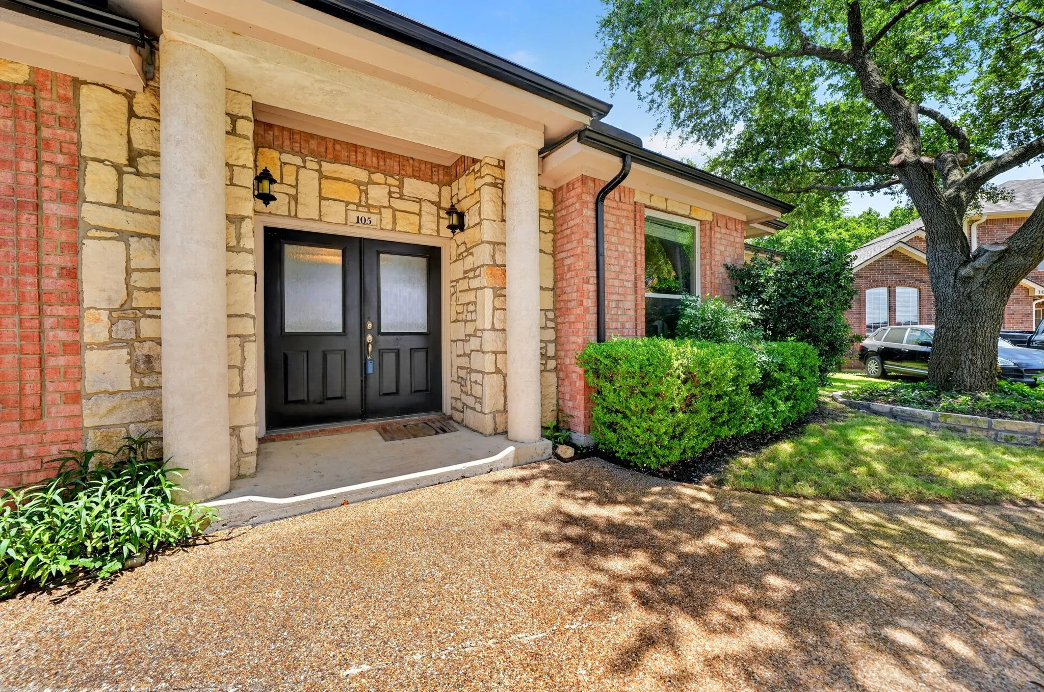 Stone and brick facade with a covered entry, featuring double black panel doors with frosted glass inserts
