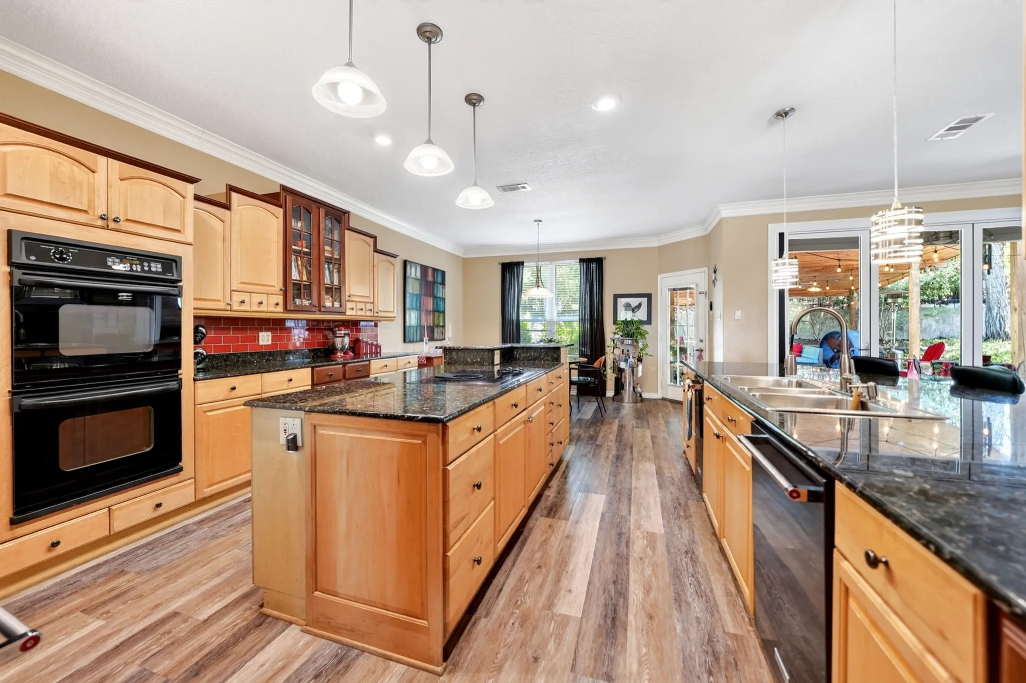 Kitchen featuring wood-finish flooring, light wood cabinetry, double wall ovens, granite countertops, and a red tile backsplash