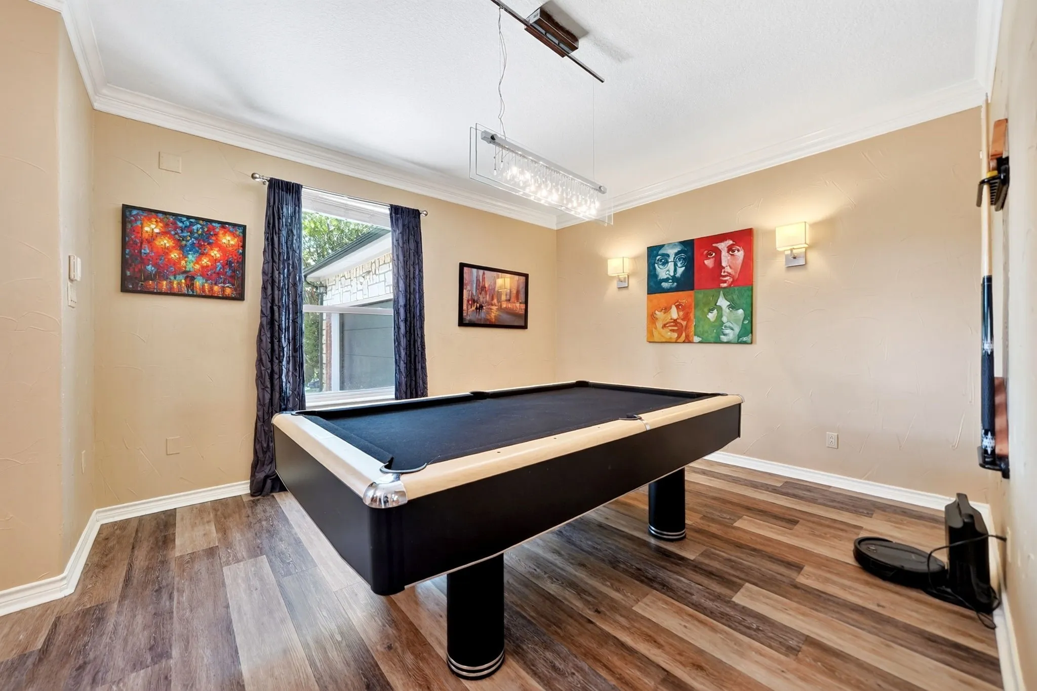 Spacious room featuring wood-finish flooring, crown molding, a large window, wall sconces, and a linear chandelier