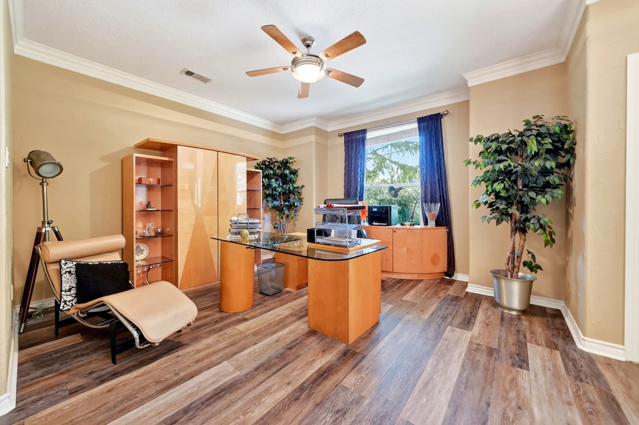 Spacious interior room featuring wood-finish flooring, a ceiling fan, crown molding, and a large window with ample natural light