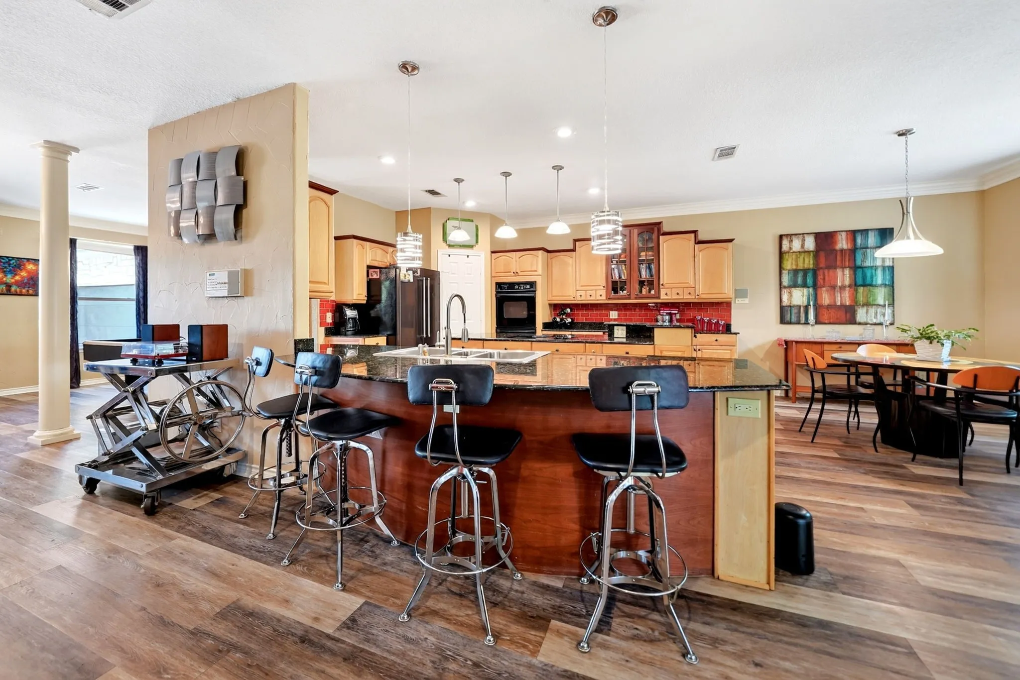Spacious open-concept kitchen featuring an island with a breakfast bar, granite countertops, wood-finish flooring, recessed lighting, and pendant lighting fixtures