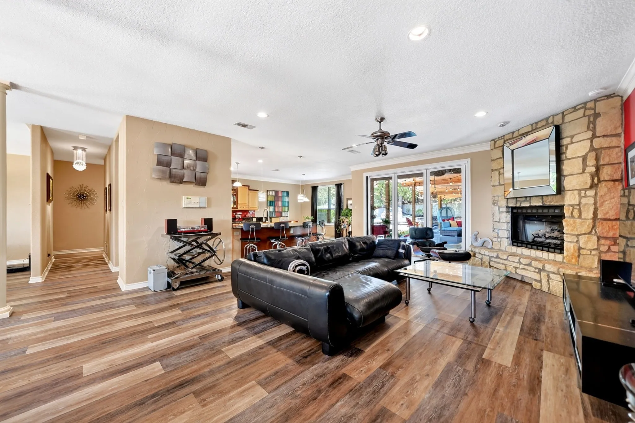 Spacious living area featuring wood-finish flooring, a stone-clad fireplace with a hearth, recessed lighting, and a ceiling fan