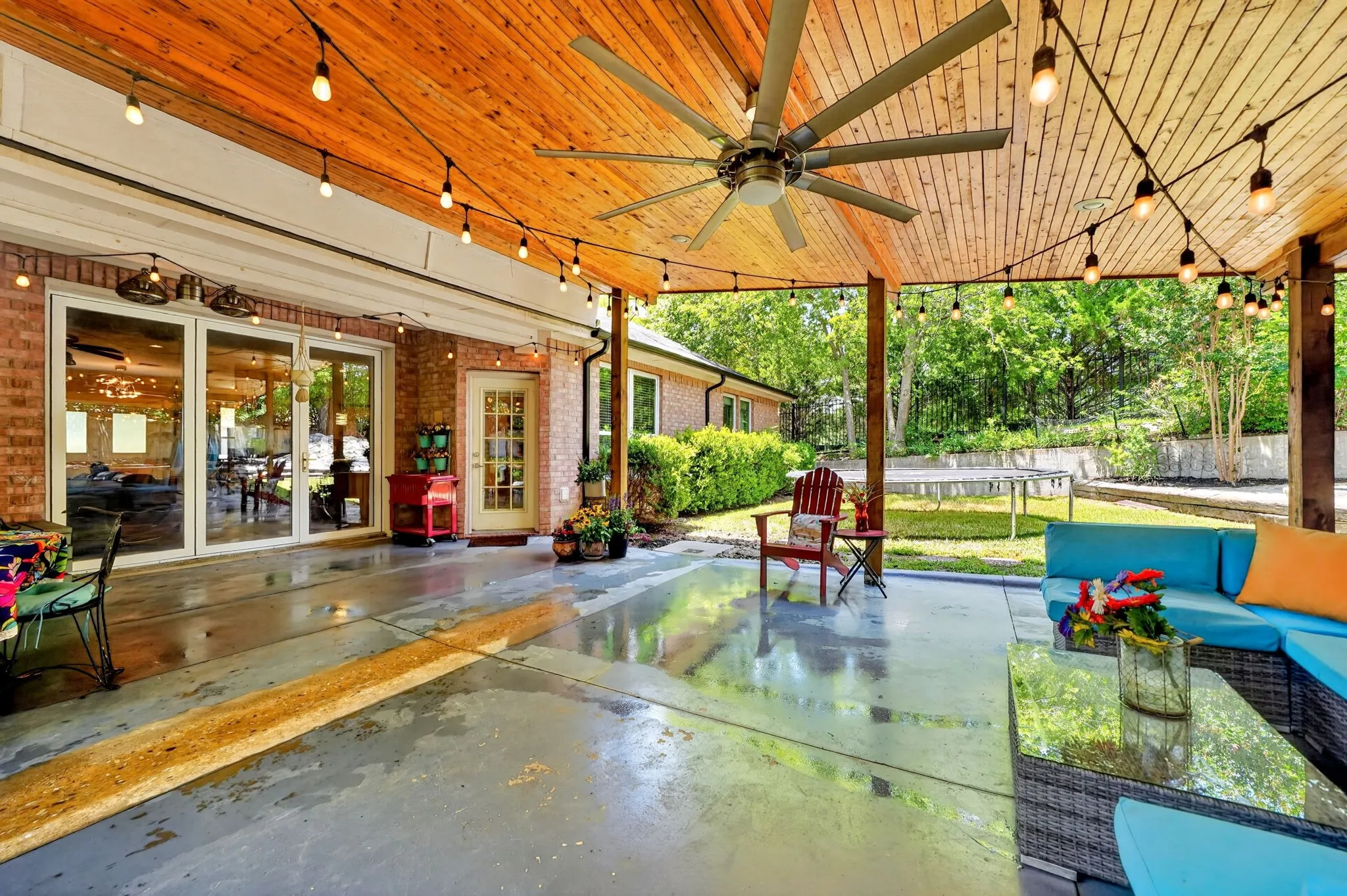 Expansive covered patio featuring a wood-finish ceiling, exposed beams, and a large ceiling fan. Doors open to the house and the whole wall opens up.