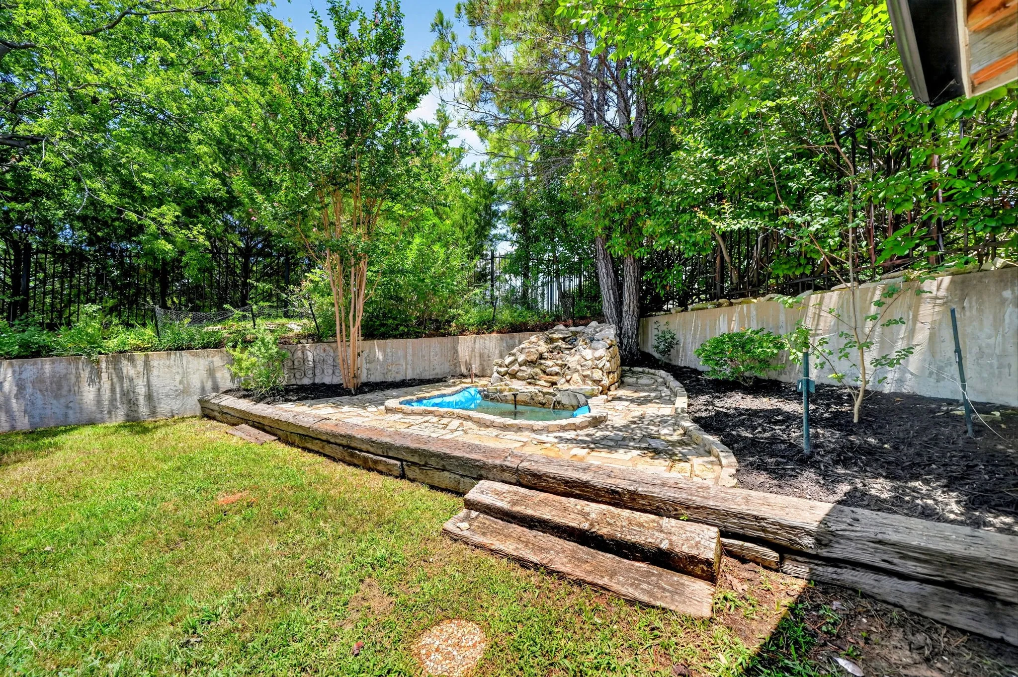 Terraced backyard featuring a stone water feature, lush landscaping, and a retaining wall