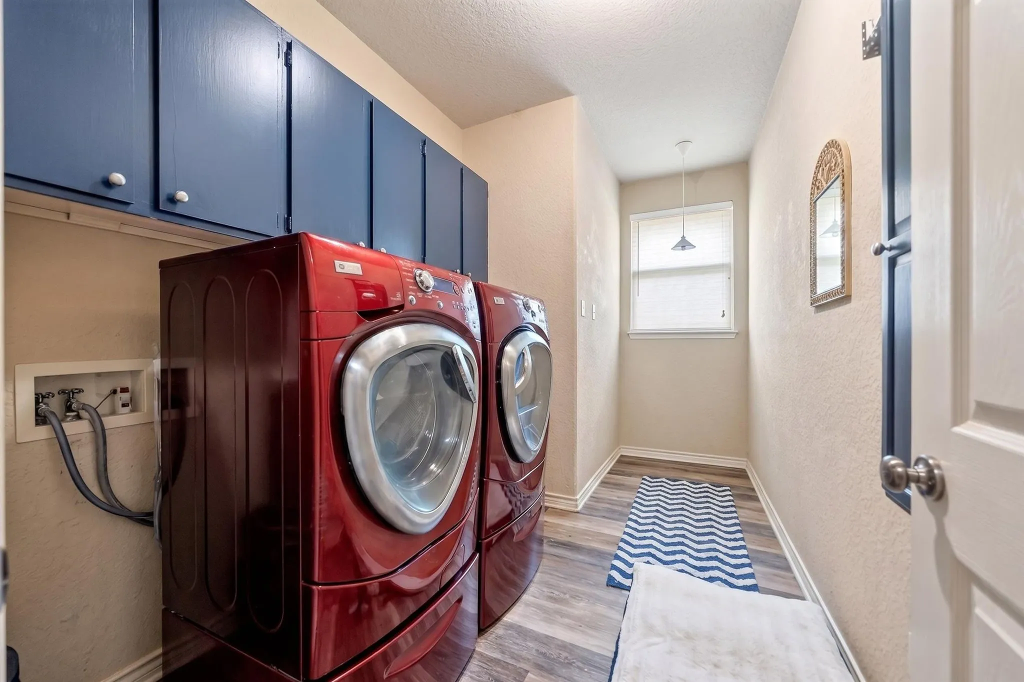Laundry area featuring wood-finish flooring, overhead blue cabinetry, sink, and a window with blinds