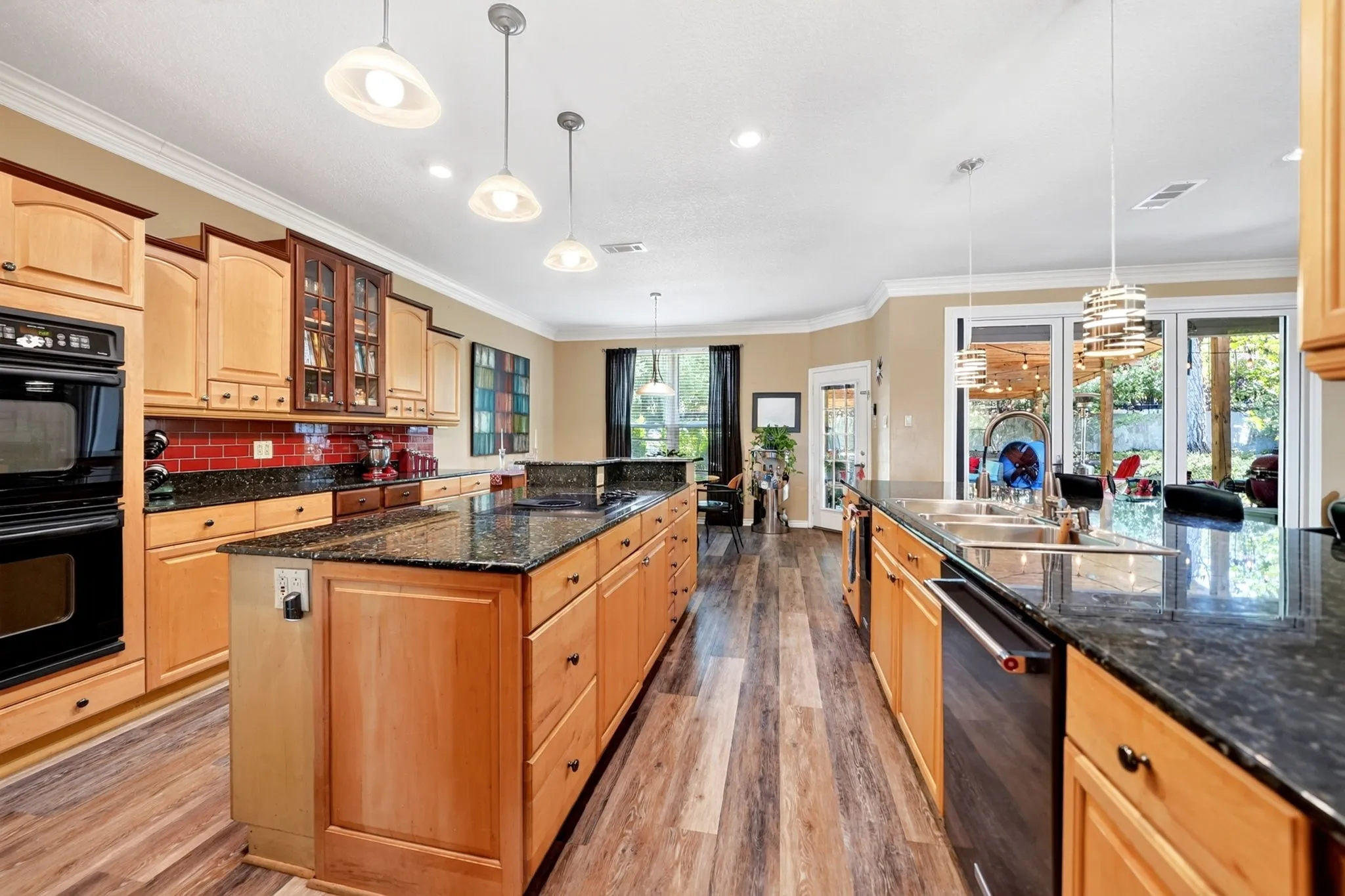 Spacious kitchen featuring a large central island, granite countertops, wood-finish flooring, light wood cabinetry, and a black double oven