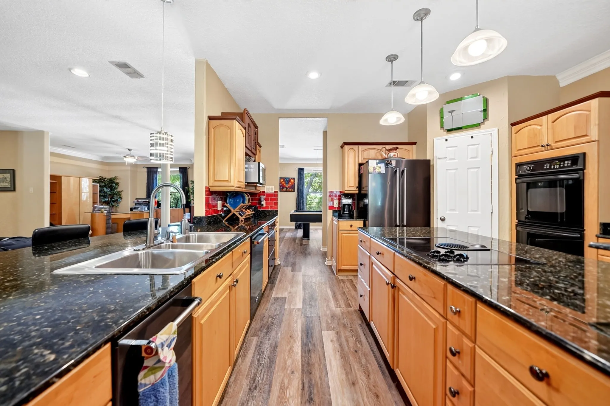 Spacious kitchen featuring dark speckled countertops, light wood cabinetry, stainless steel appliances, and wood-finish flooring