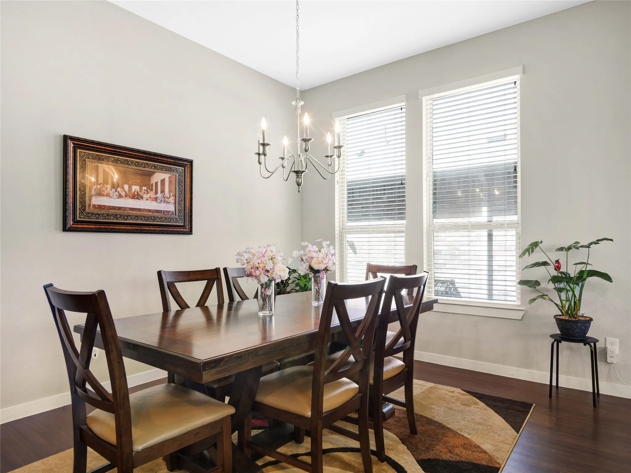 Dining area featuring a classic chandelier, wood-finish flooring, and two tall windows with blinds