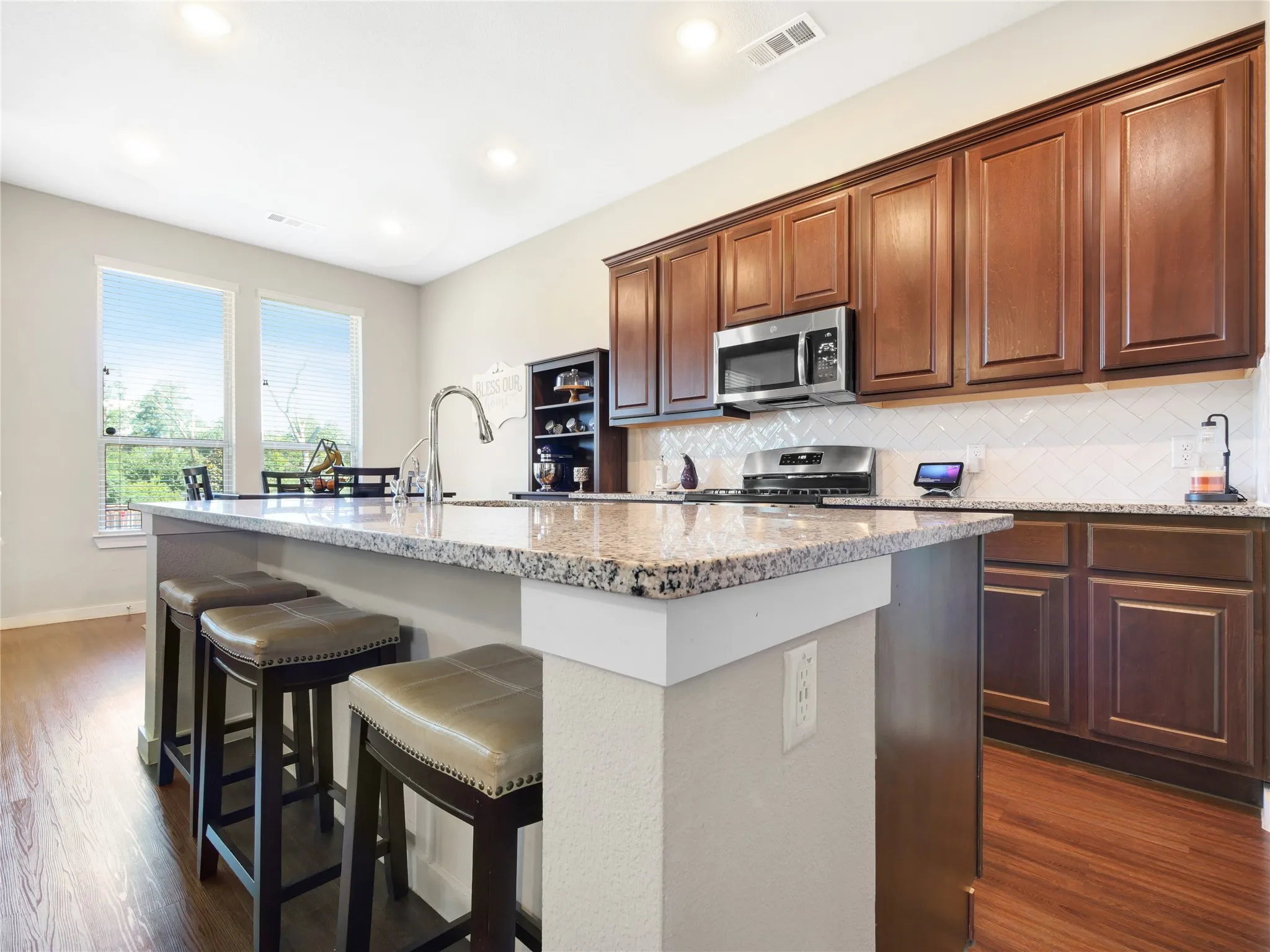 Kitchen featuring a large island with a gooseneck faucet, granite countertops, rich wood-finish cabinetry, stainless steel appliances, and wood-finish flooring