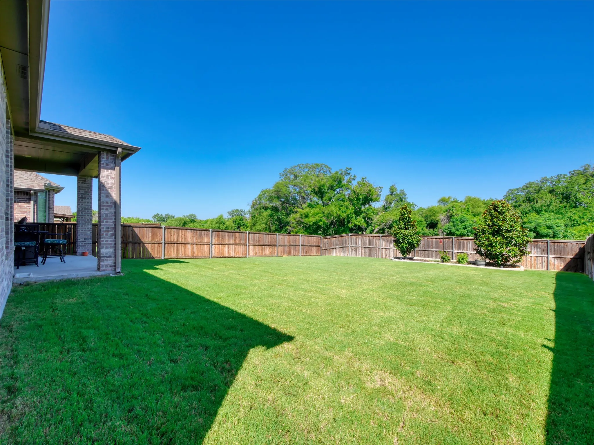 Expansive backyard featuring a manicured lawn, full privacy fencing, and two mature ornamental trees