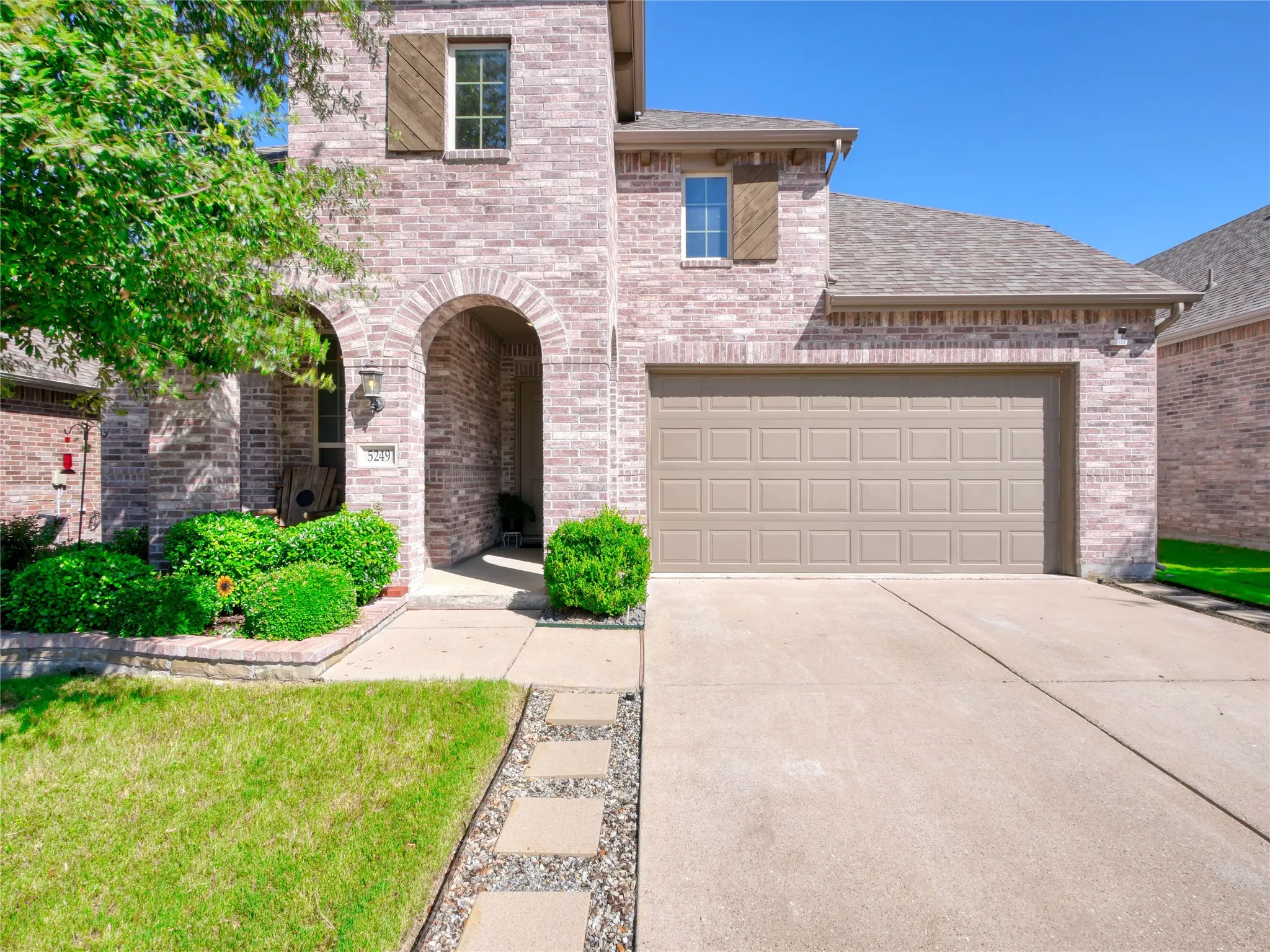 Brick facade with arched entryway, a single-car garage, and mature landscaping