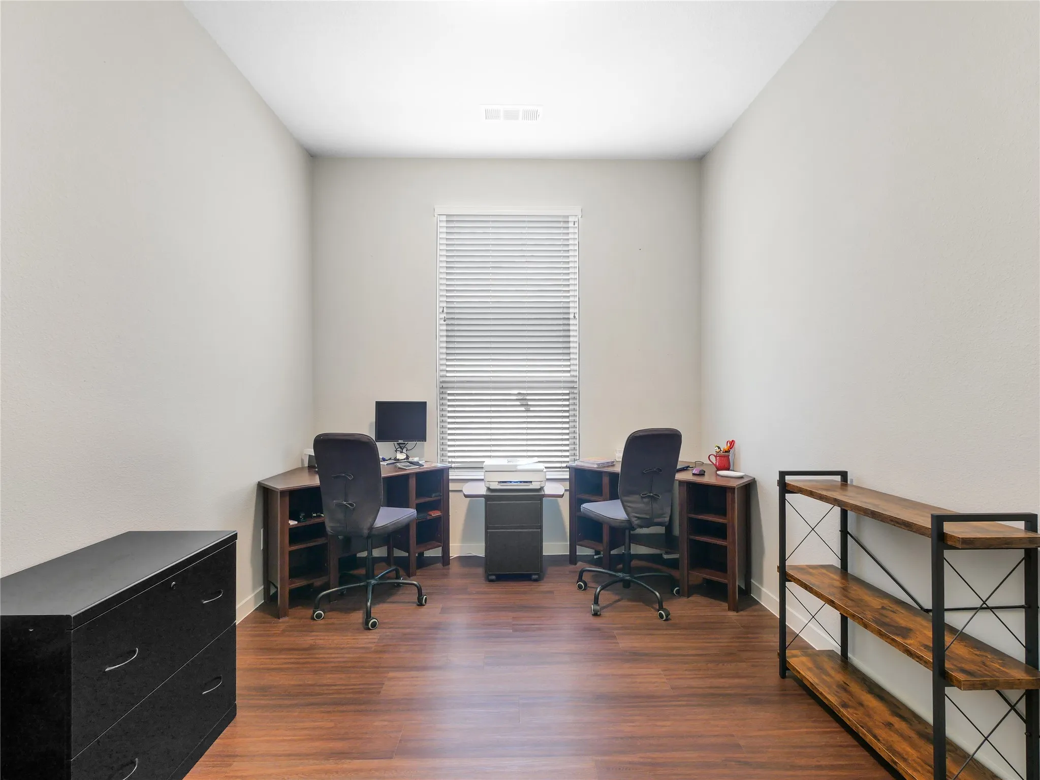Spacious room featuring wood-finish flooring, light neutral wall paint, and a single window with horizontal blinds