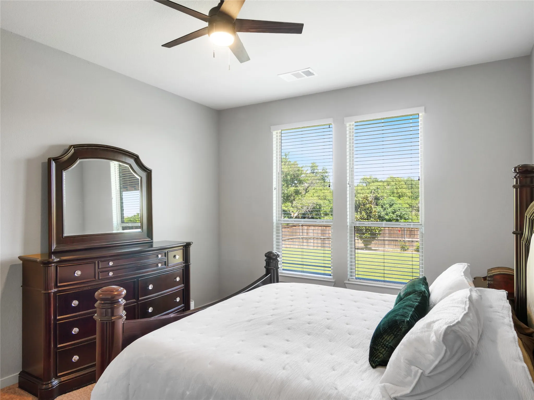 Bright room featuring two windows with blinds, a ceiling fan with integrated lighting, and neutral wall paint