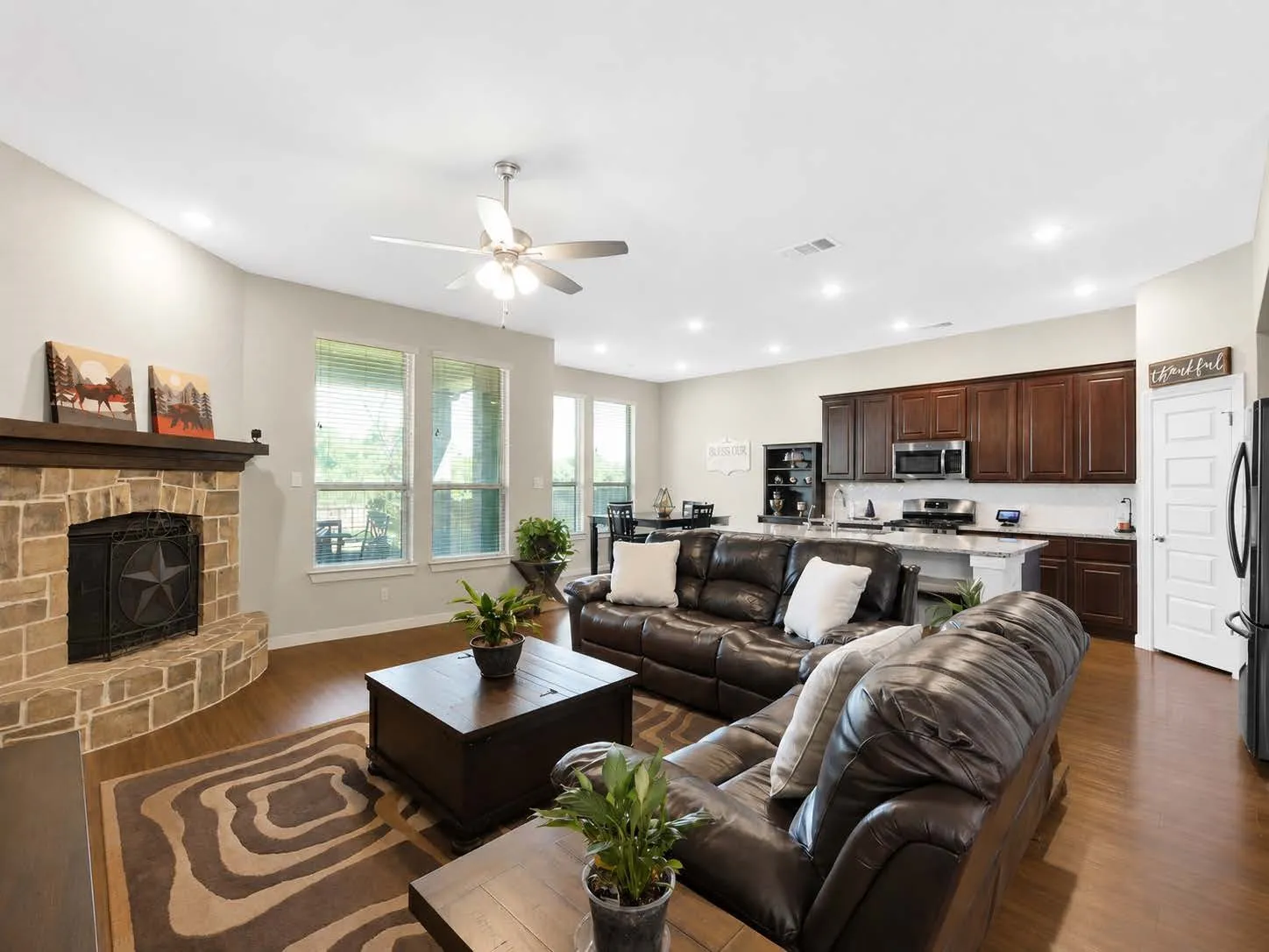 Open-concept living space featuring wood-finish flooring, a stone fireplace with a wood mantle, and multiple windows