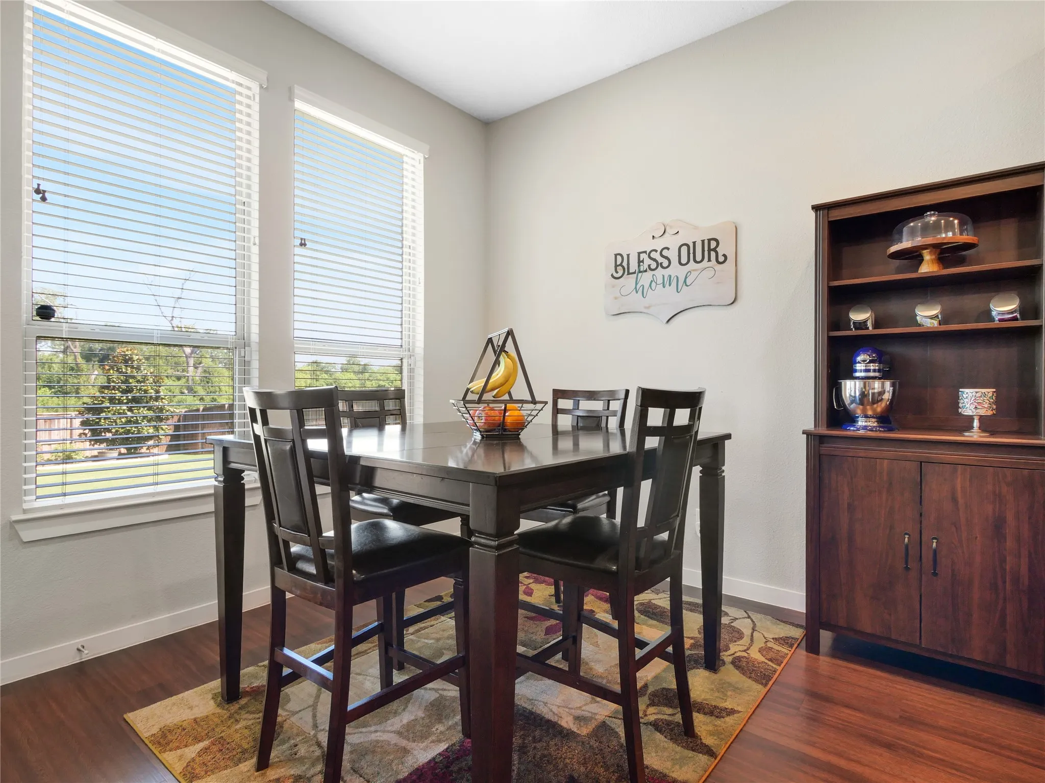 Dining area featuring two large windows with blinds, wood-finish flooring, and a built-in wooden cabinet with shelving