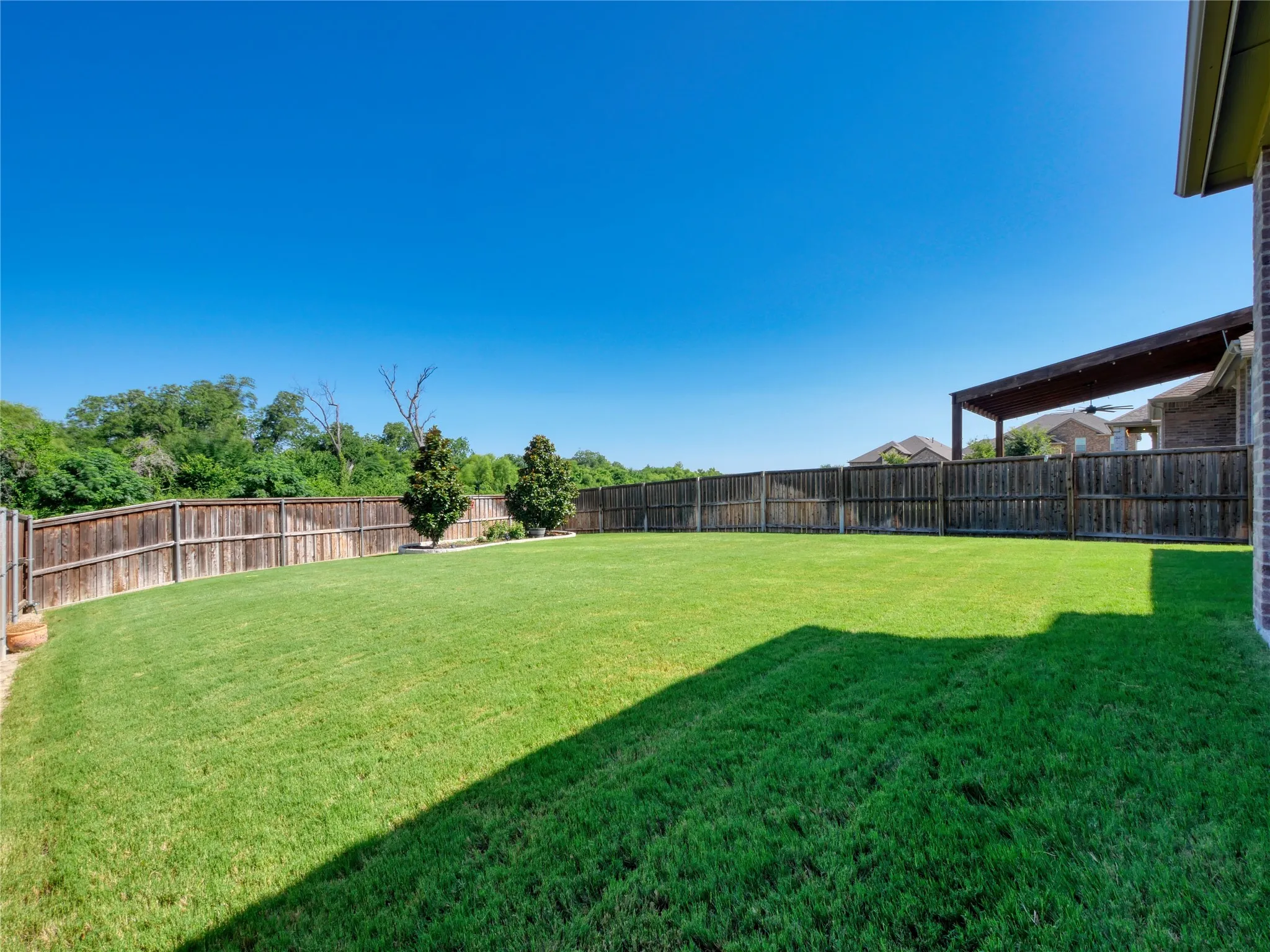 Expansive fenced backyard featuring a substantial lawn area and a covered patio structure