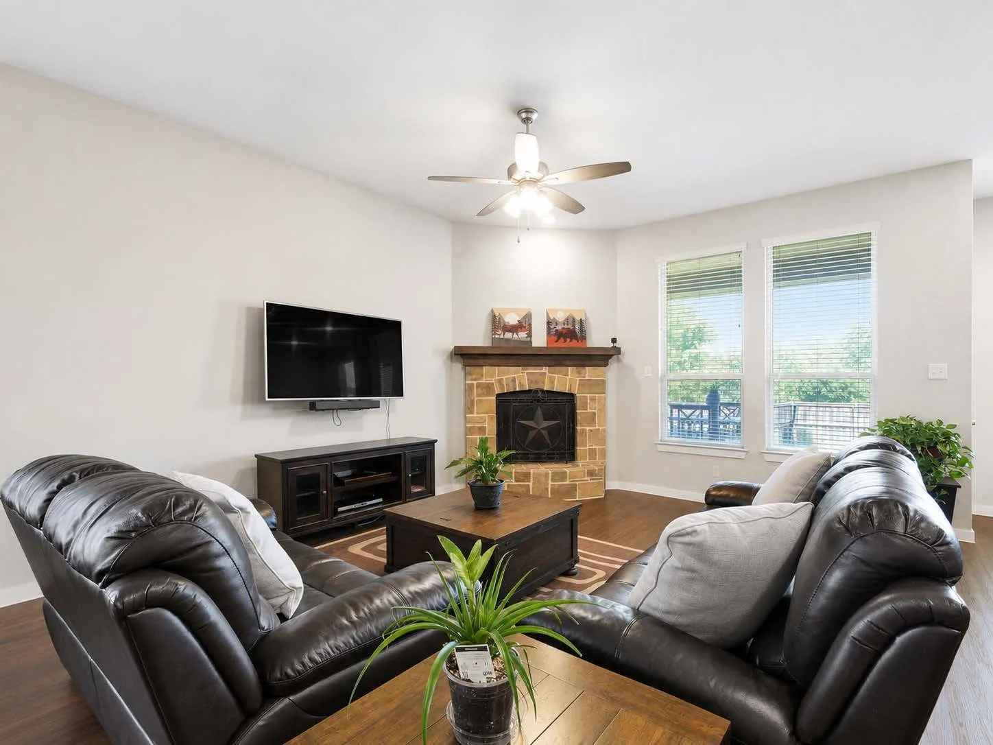 Living area featuring wood-finish flooring, a stone fireplace with a wood mantle, and two large windows