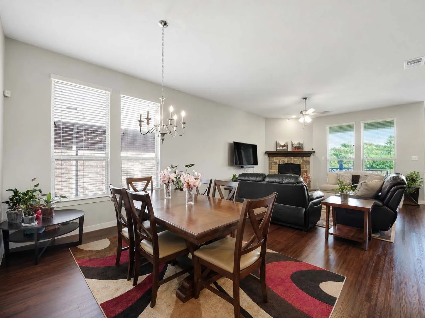 Open-concept living space featuring wood-finish flooring, a stone-surround fireplace with a wood mantle, and multiple windows