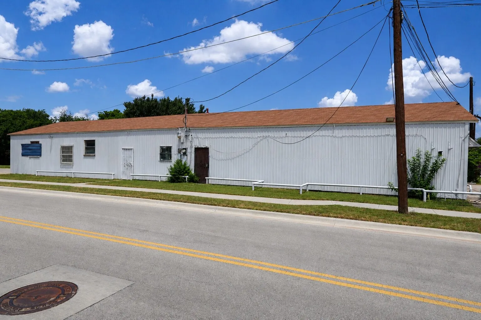 Long rectangular building with a brown shingle roof and white corrugated siding