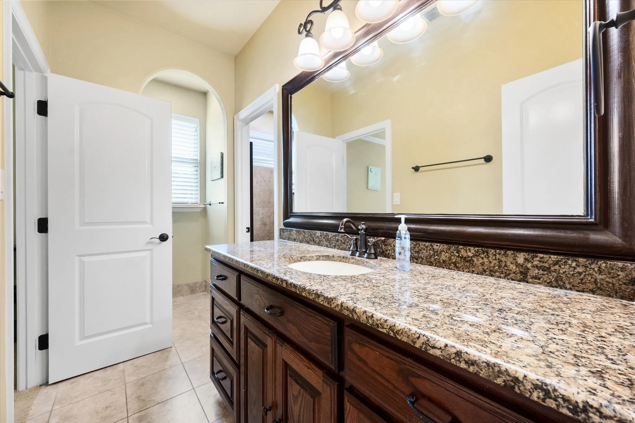 Spacious Jack and Jill bathroom with vanity featuring a granite countertop, undermount sink, and dark wood cabinetry