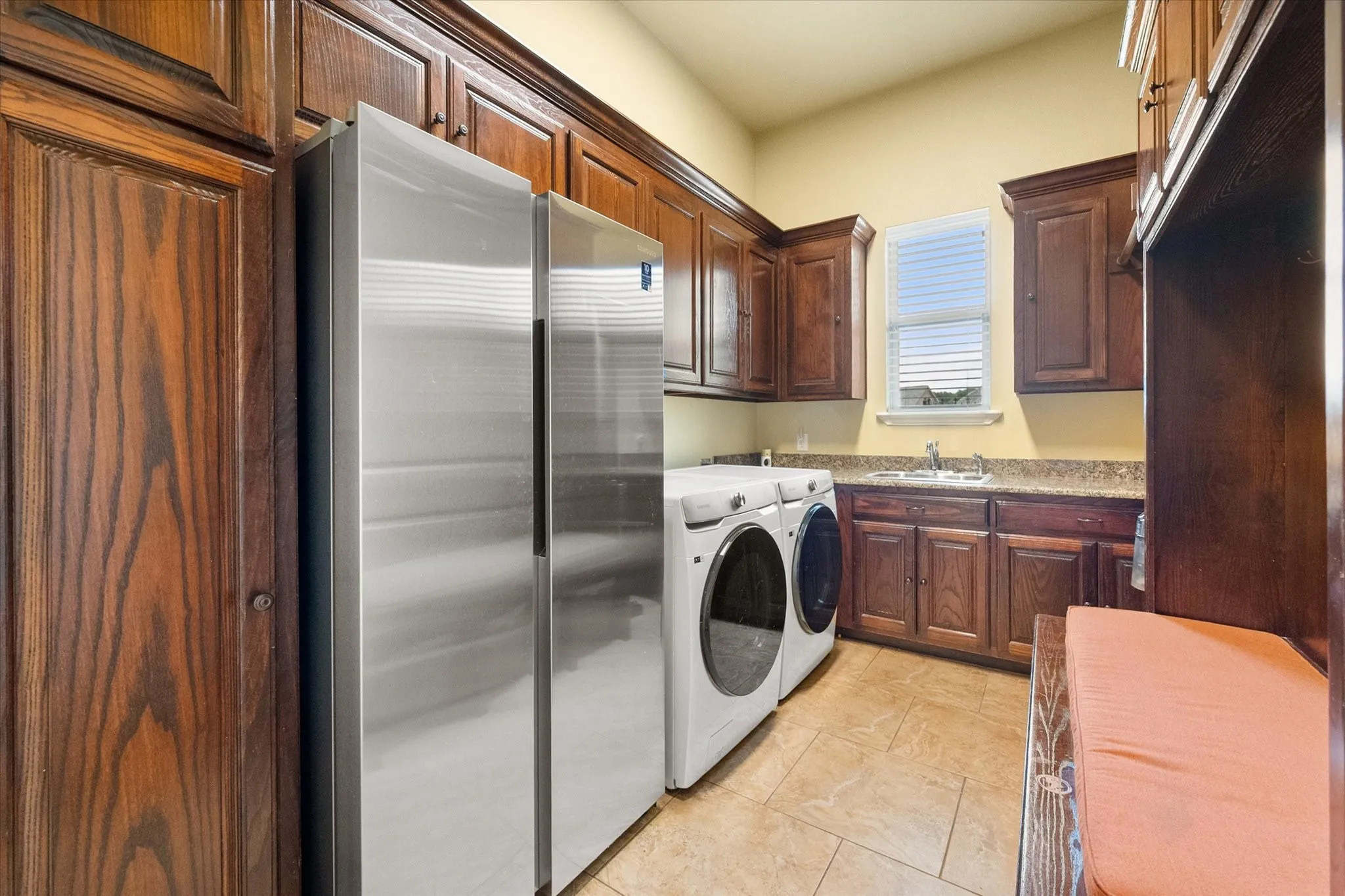 Utility room featuring extensive wood cabinetry, tile flooring, a built-in sink with a countertop, and a window for natural light
