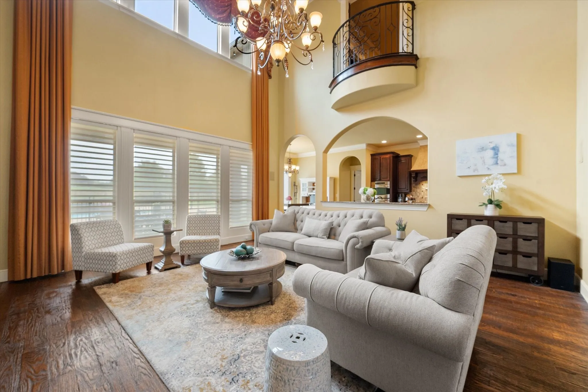 Two-story living area featuring wood-finish flooring, a grand chandelier, and expansive windows with custom window treatments