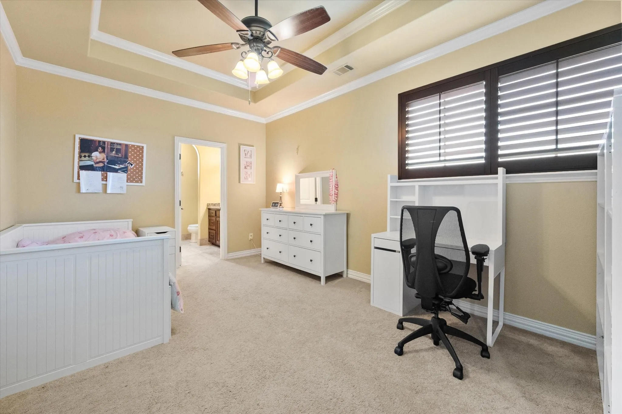 Carpeted interior space featuring a tray ceiling, ceiling fan with light fixture, and window with dark wood trim and horizontal blinds