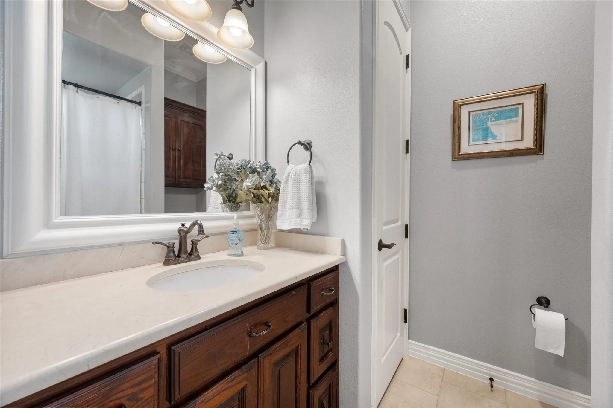 Bathroom vanity featuring a light-toned countertop with an undermount sink, bronze-finish faucet, and a large framed mirror
