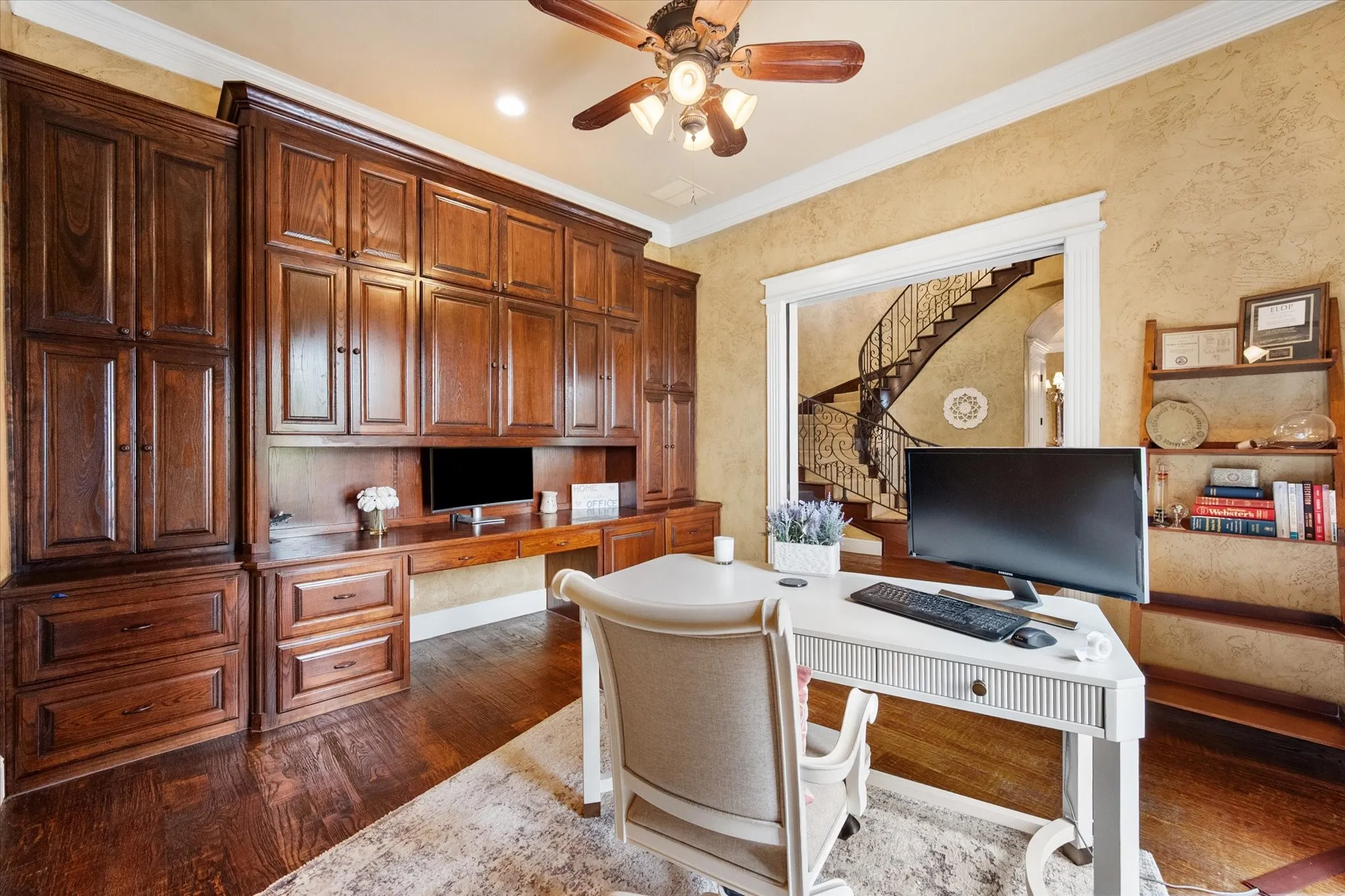 Dedicated workspace featuring extensive built-in cabinetry, rich wood-finish flooring, textured wall finishes, and a ceiling fan