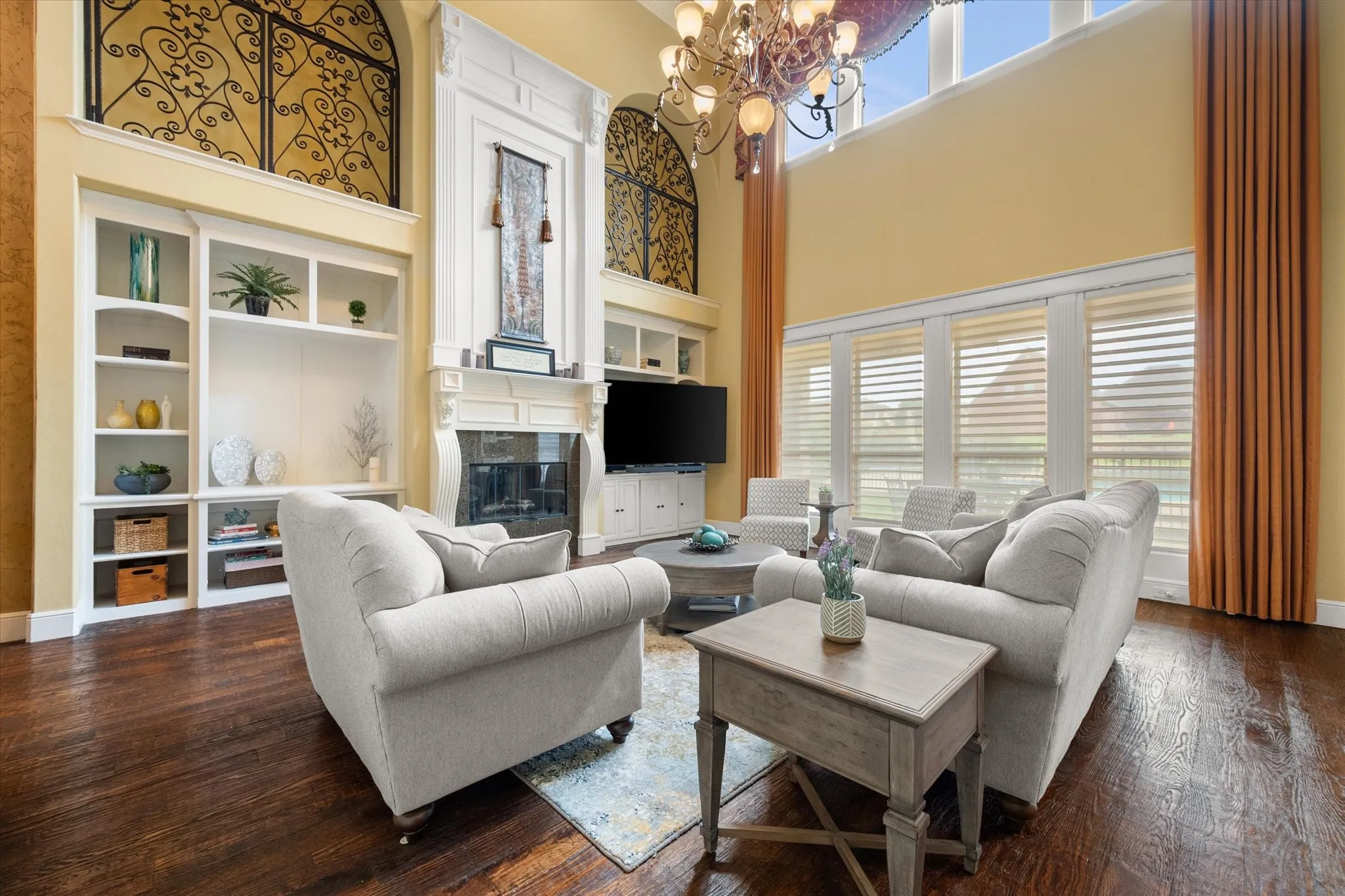 Grand living area featuring soaring ceilings, dark wood-finish flooring, a built-in media center with shelving, a detailed fireplace surround, and arched niches with decorative ironwork
