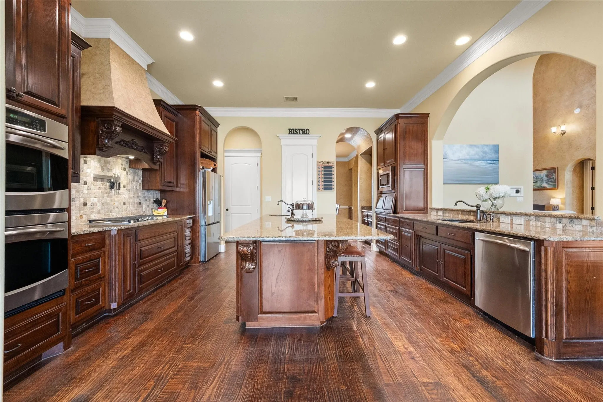Spacious kitchen featuring rich wood-finish flooring, custom cabinetry, stainless steel appliances, a center island with bar seating, and granite countertops