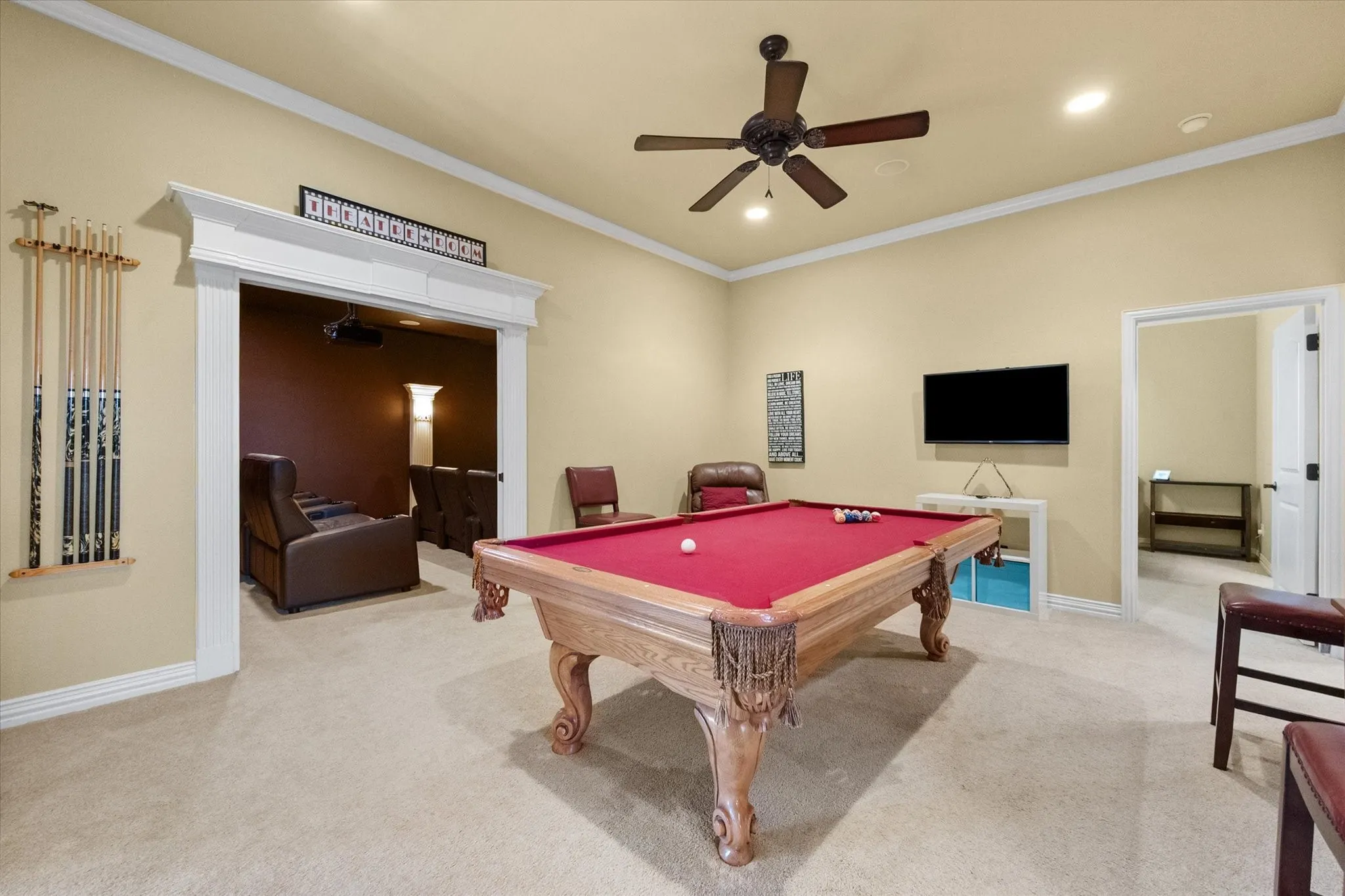 Carpeted entertainment area featuring a billiard table, ceiling fan with light fixture, and crown molding
