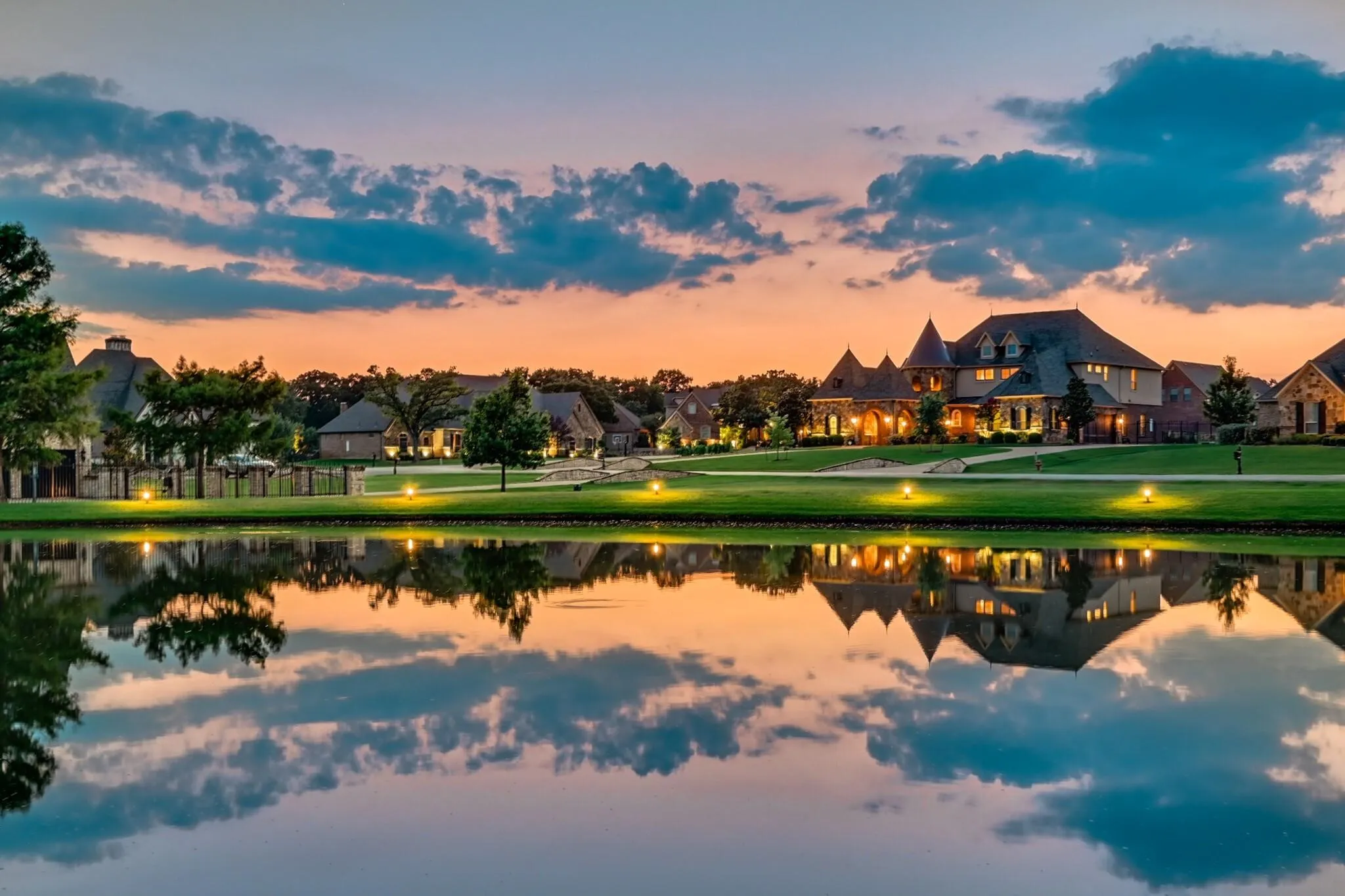 Expansive community pond featuring a manicured lawn, established trees, and comprehensive exterior lighting