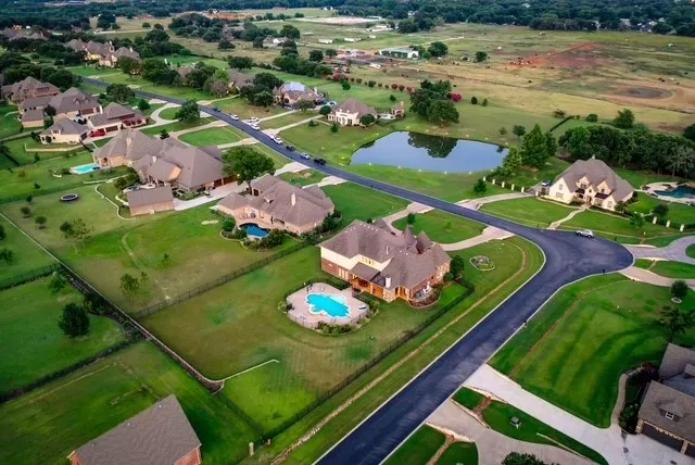 Aerial perspective showcasing residential properties with expansive green lawns, paved streets, a private swimming pool, and a natural pond feature