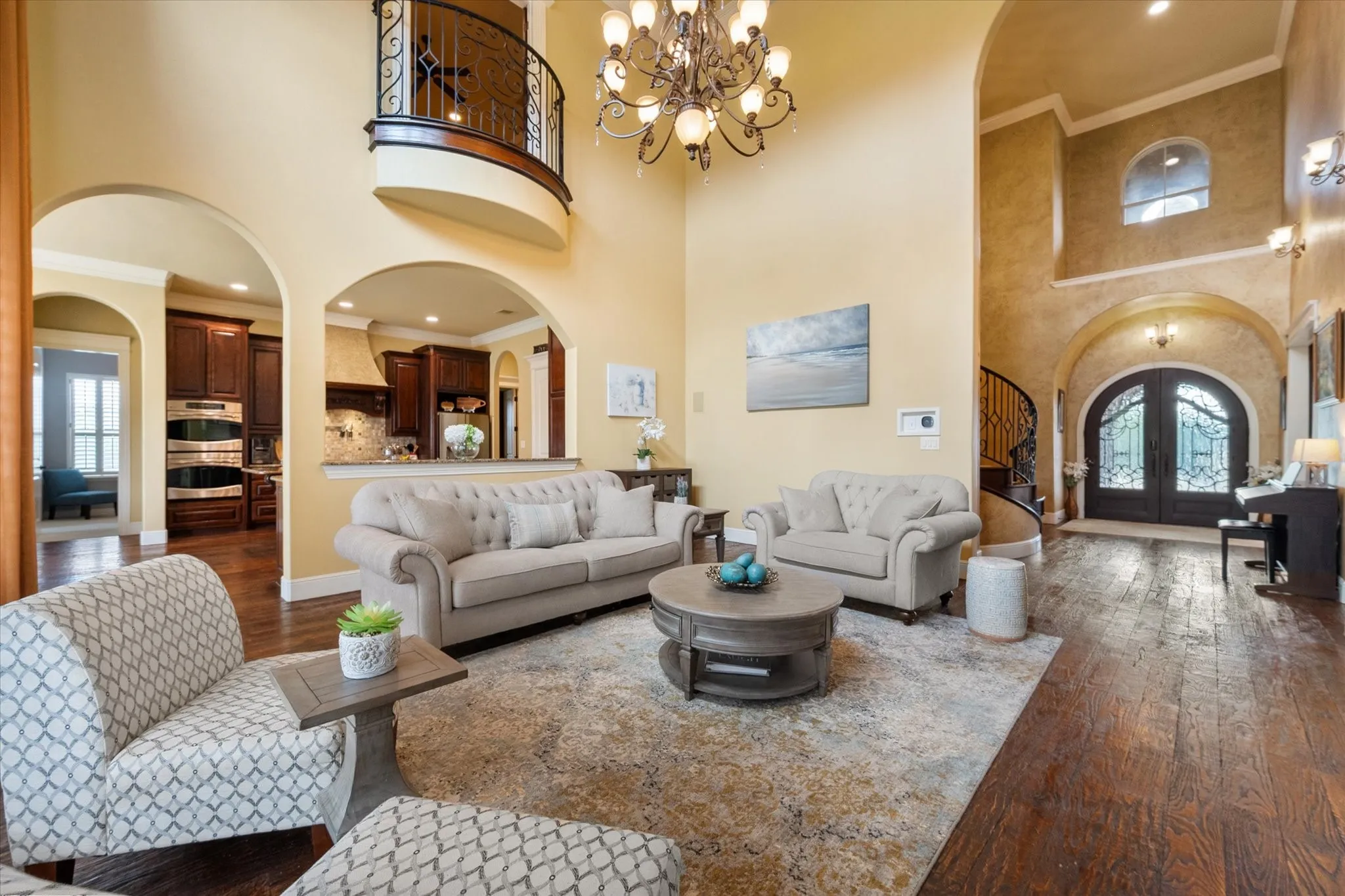 Two-story living area with wood-finish flooring, a grand chandelier, and arched doorways