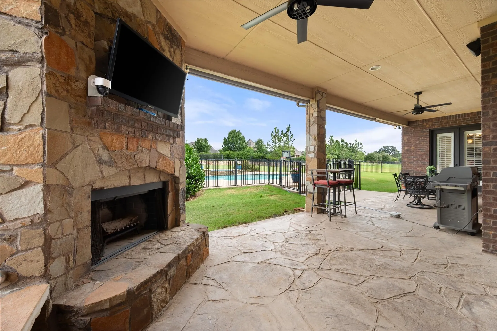 Covered patio featuring a stone fireplace, integrated television, and ceiling fans