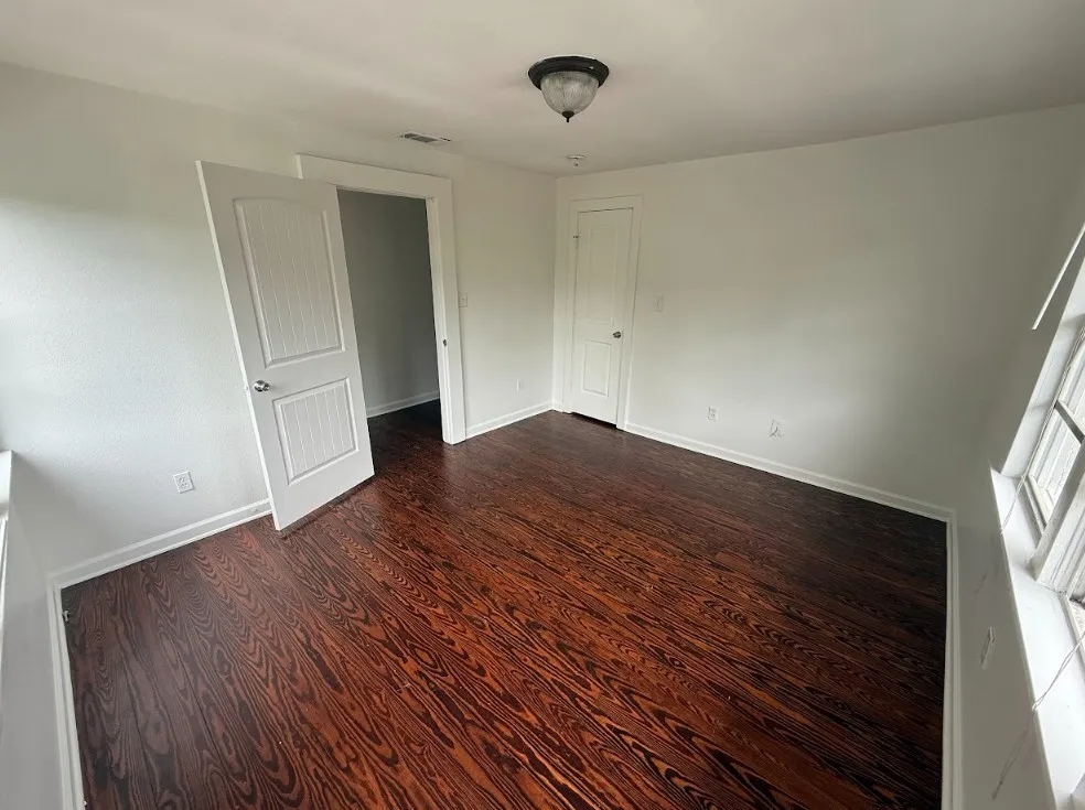 Spacious room featuring rich wood-finish flooring, crisp white walls, and a semi-flush mount ceiling light fixture