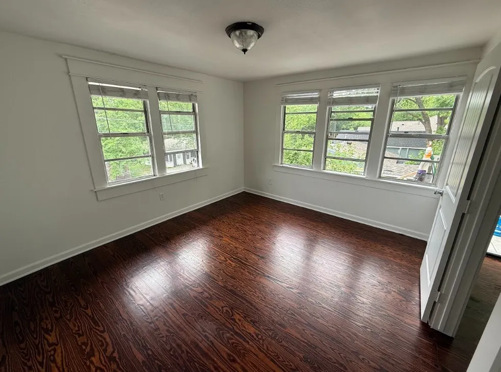Room featuring rich wood-finish flooring, white trim, multiple windows with white blinds, and a flush mount ceiling light fixture